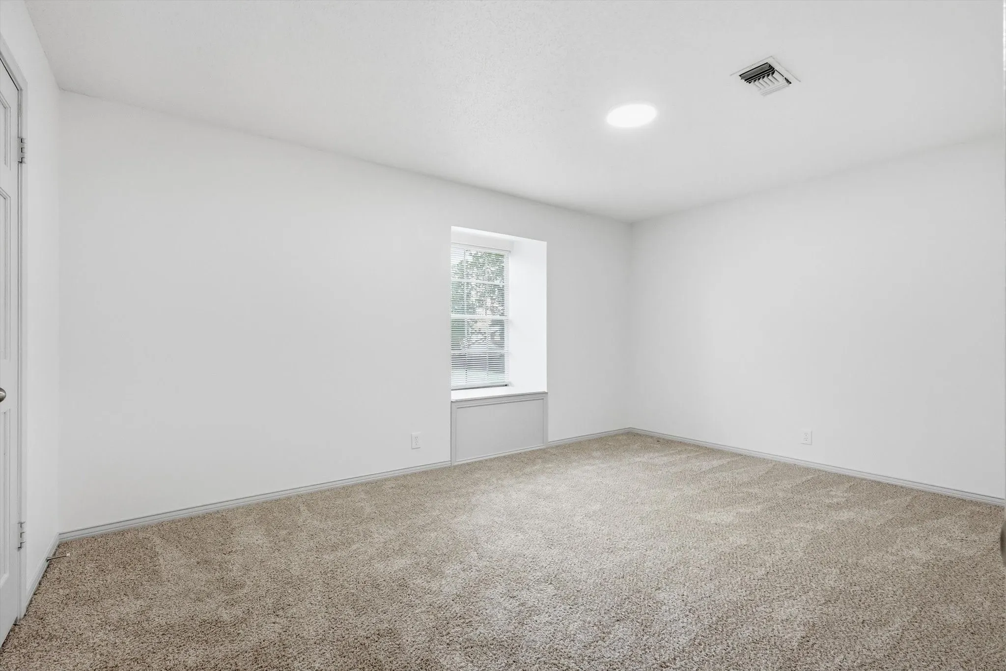 Neutral tone wall paint, light-colored carpet flooring, recessed ceiling light, ceiling-mounted air vent, and a window with a built-in window seat