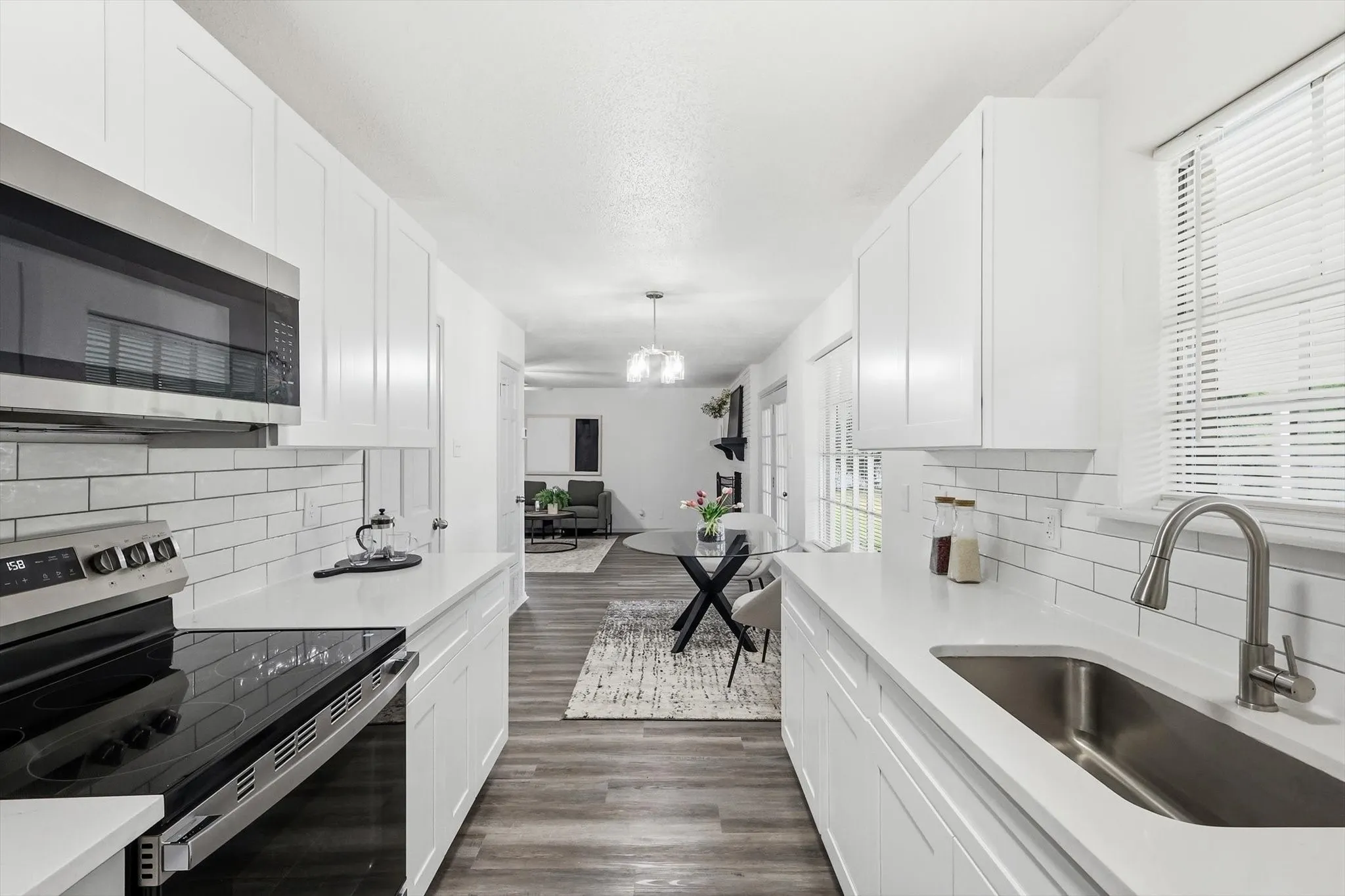 Galley kitchen featuring white shaker cabinetry, white subway tile backsplash, stainless steel appliances, quartz countertops, and wood-finish flooring