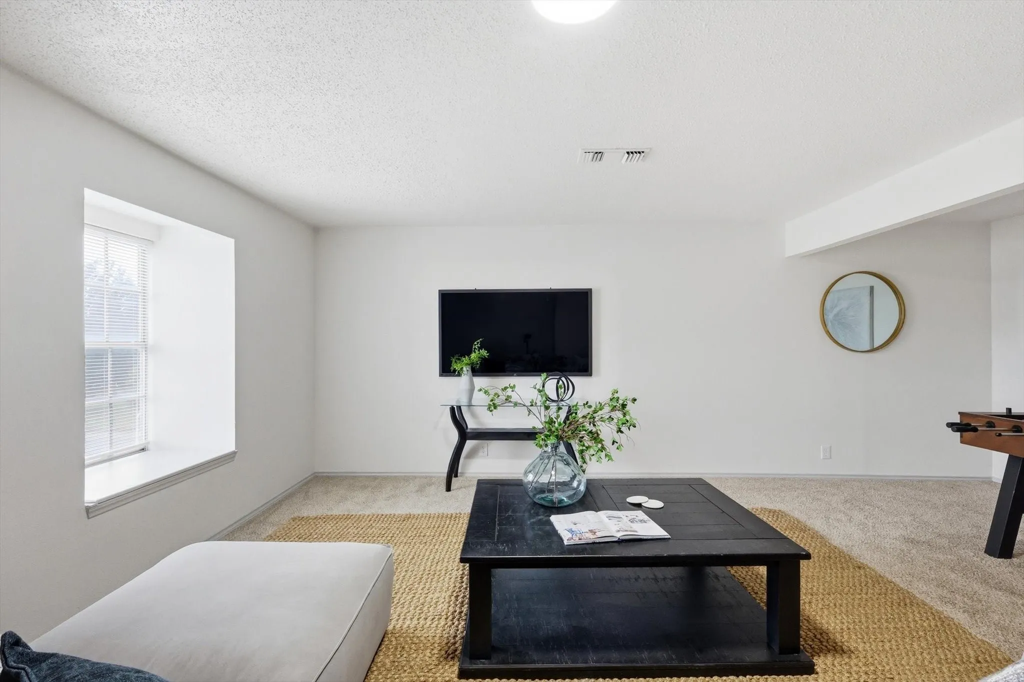 Spacious living area featuring neutral carpeting, white walls, a large window, recessed lighting, and a broad ceiling beam