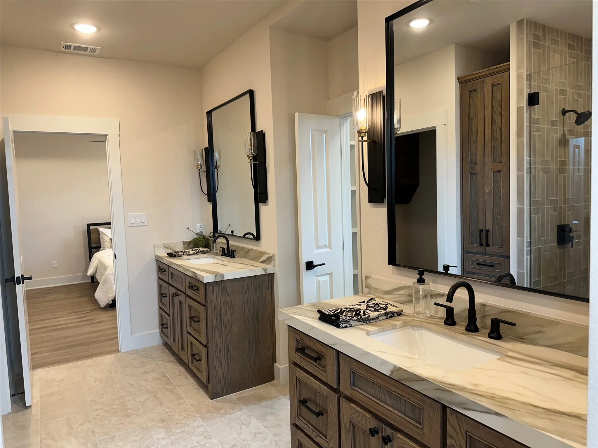 Bathroom featuring dual vanities with wood-finish cabinetry, white countertops with natural veining, and matte black fixtures