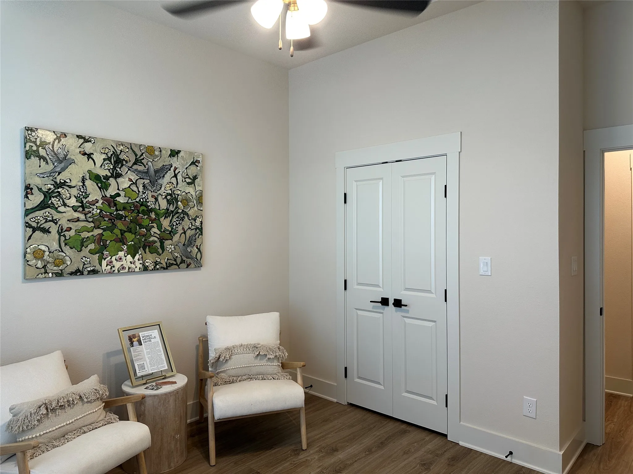 Neutral-toned room featuring a ceiling fan with integrated lighting, wood-finish flooring, white bi-fold doors, and crisp white baseboards