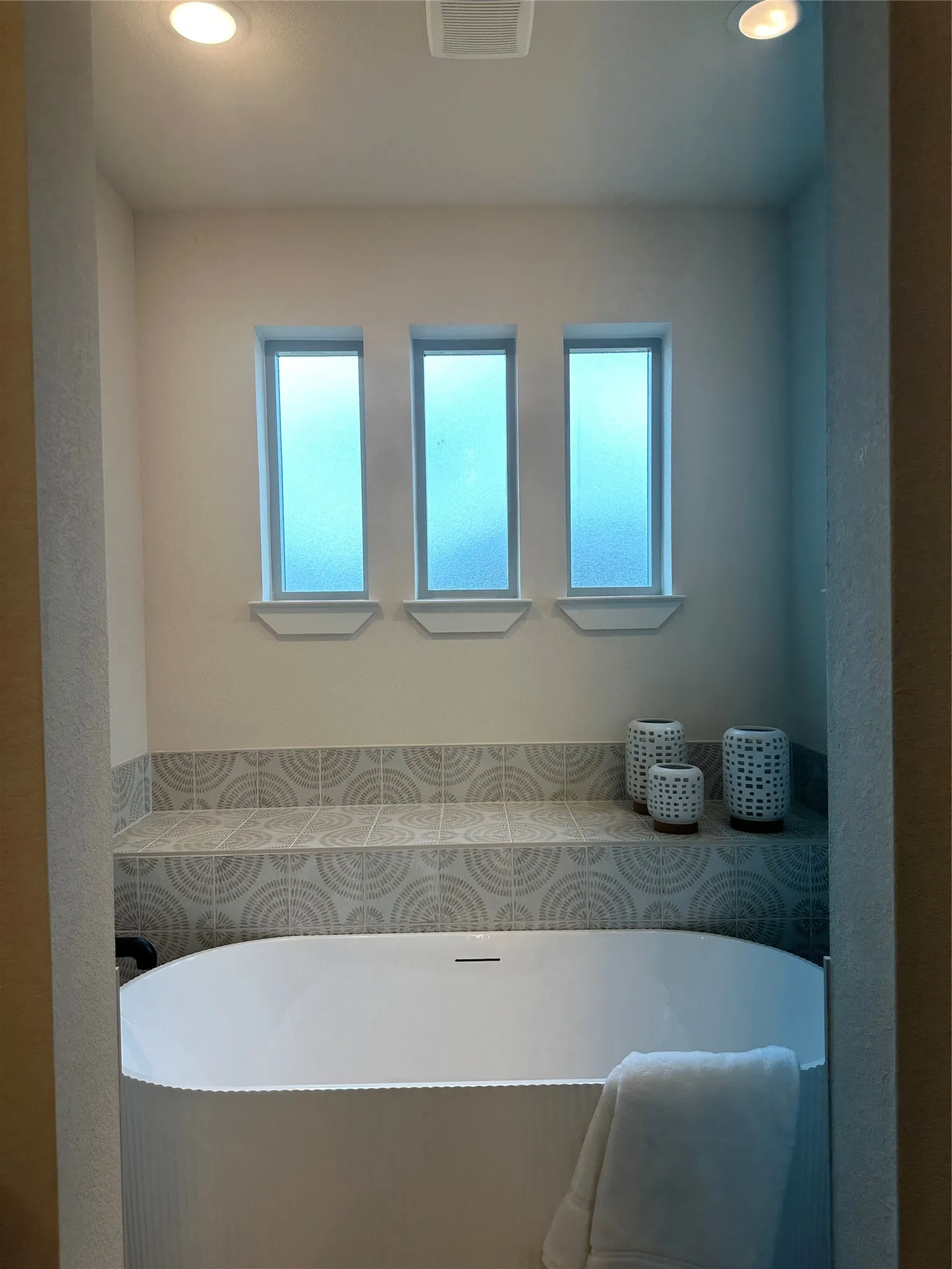 Modern freestanding tub set against a tiled wall with decorative patterns