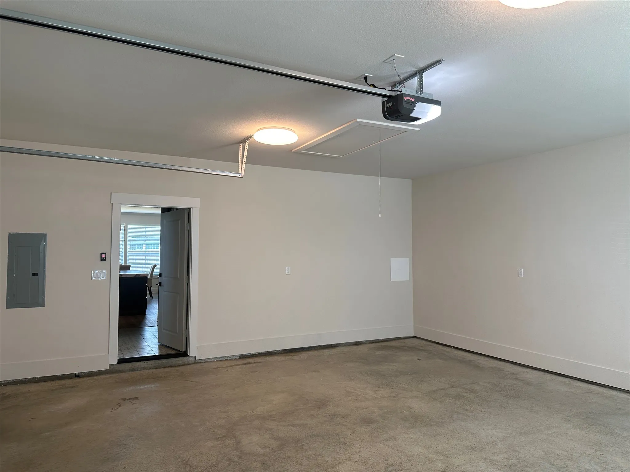 Spacious garage featuring a concrete floor, light-toned walls, overhead lighting, an automatic garage door opener, and interior access