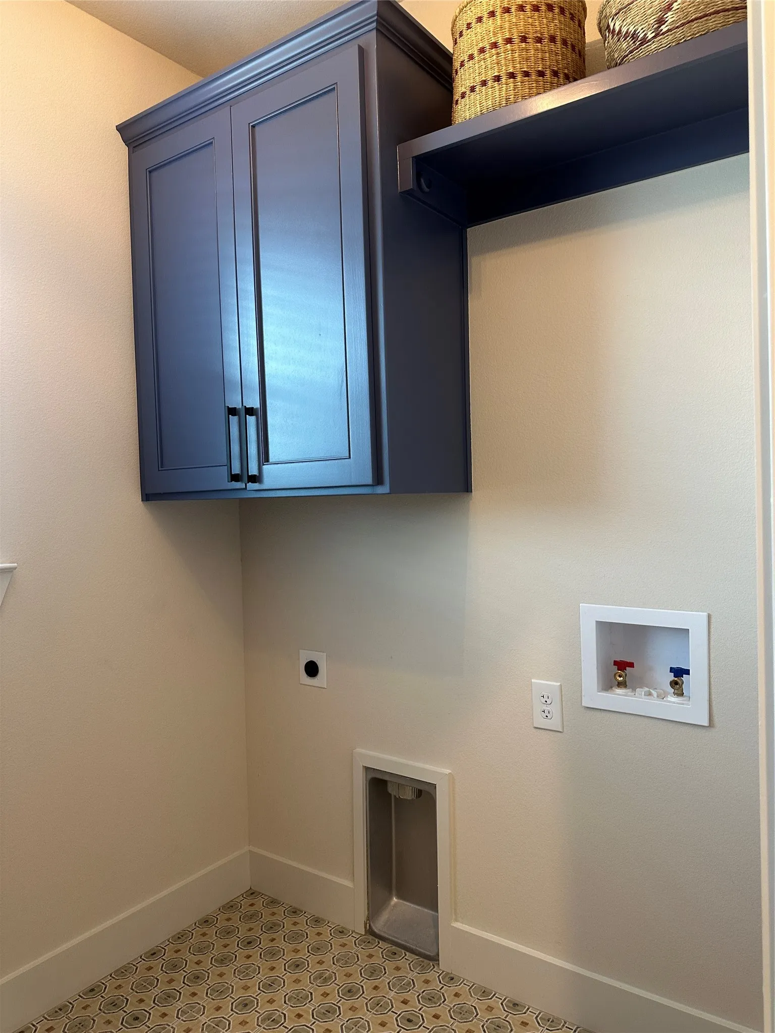 Laundry area featuring patterned tile flooring, a built-in shelf, and dark blue cabinetry with matte black hardware