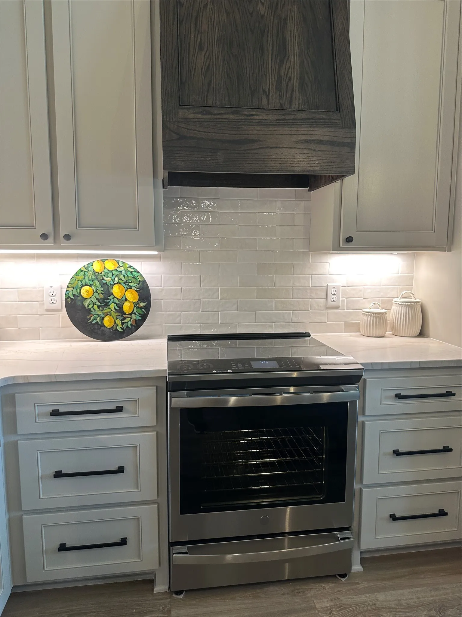Contemporary kitchen featuring a stainless steel range, light-toned shaker cabinets, and a custom wood-paneled range hood