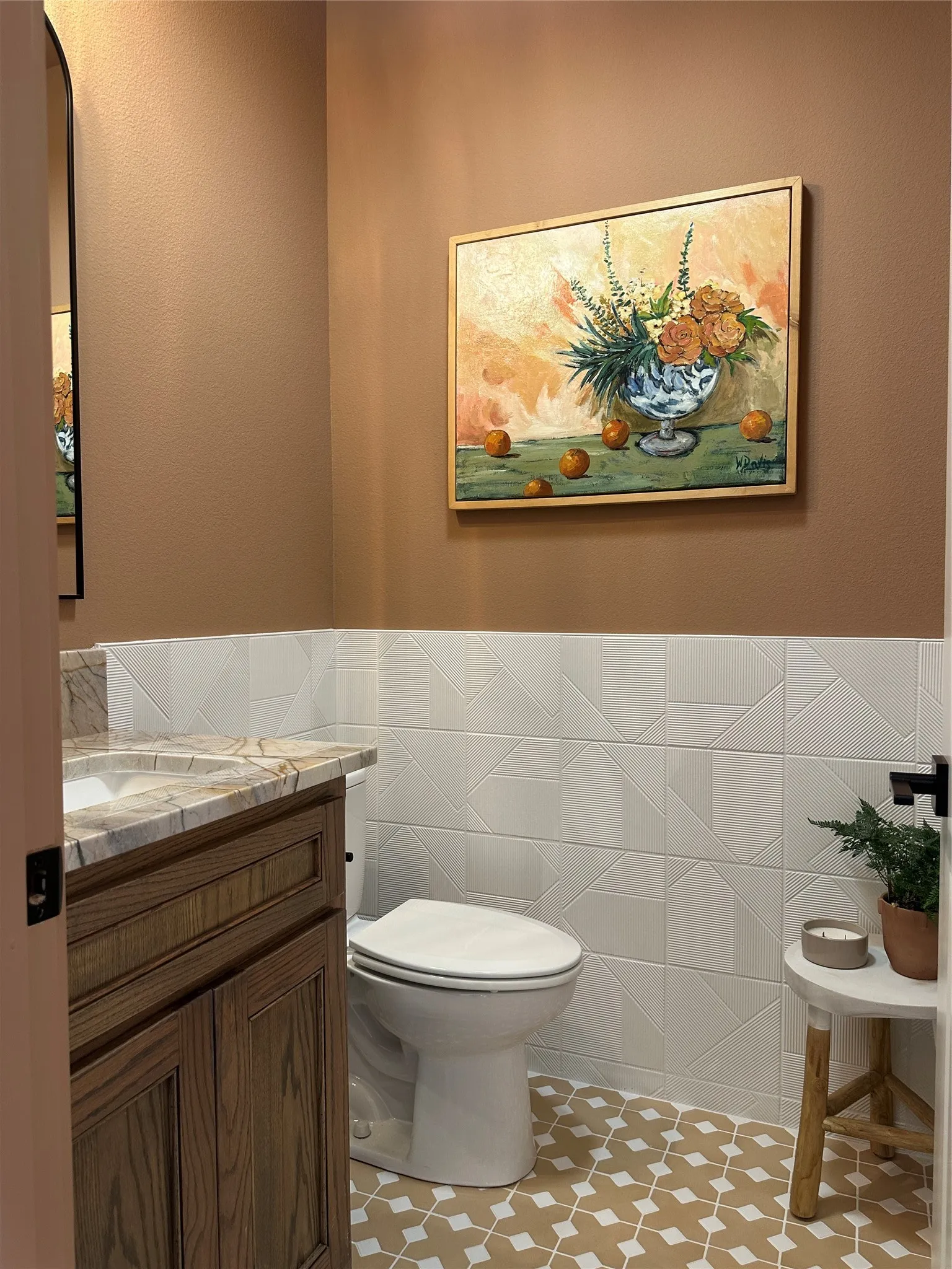 Powder room featuring a wood-finish vanity with a stone countertop, a white toilet, geometric wall tiling, and patterned floor tiling
