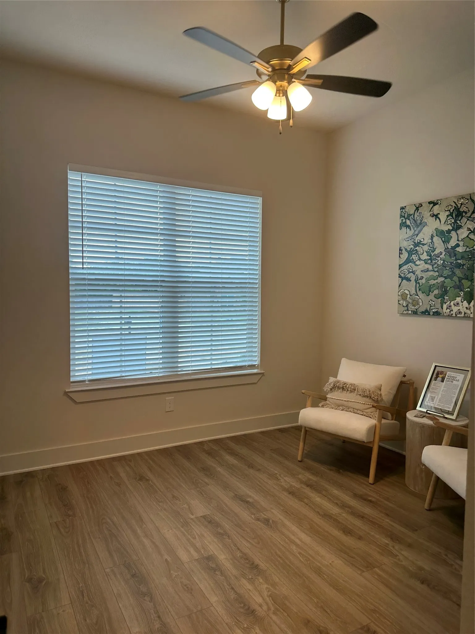 Neutral wall paint with wood-finish flooring, featuring a window with horizontal blinds, a ceiling fan with integrated lighting, and white baseboards