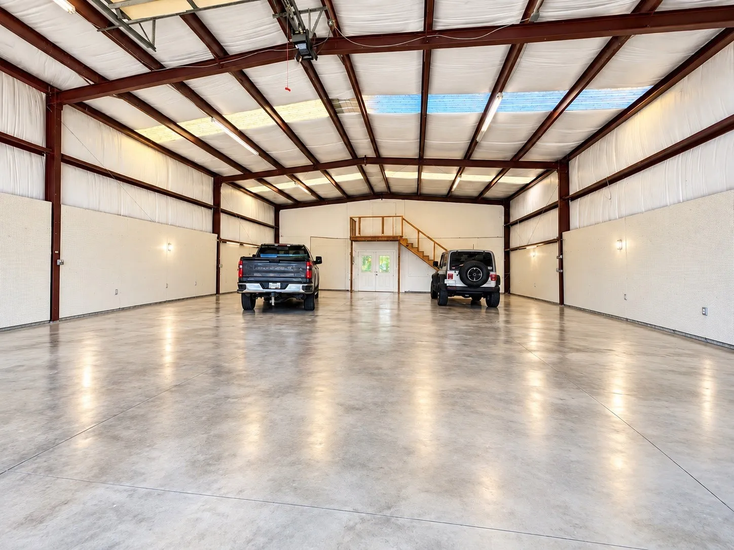 Expansive concrete flooring in a large open space with steel beam construction, insulated walls, an upper-level wood-finished platform with railing, and integrated lighting​​‌​​​​‌​​‌‌​‌‌​​​‌‌​‌​‌​‌​​​‌​​ fixtures