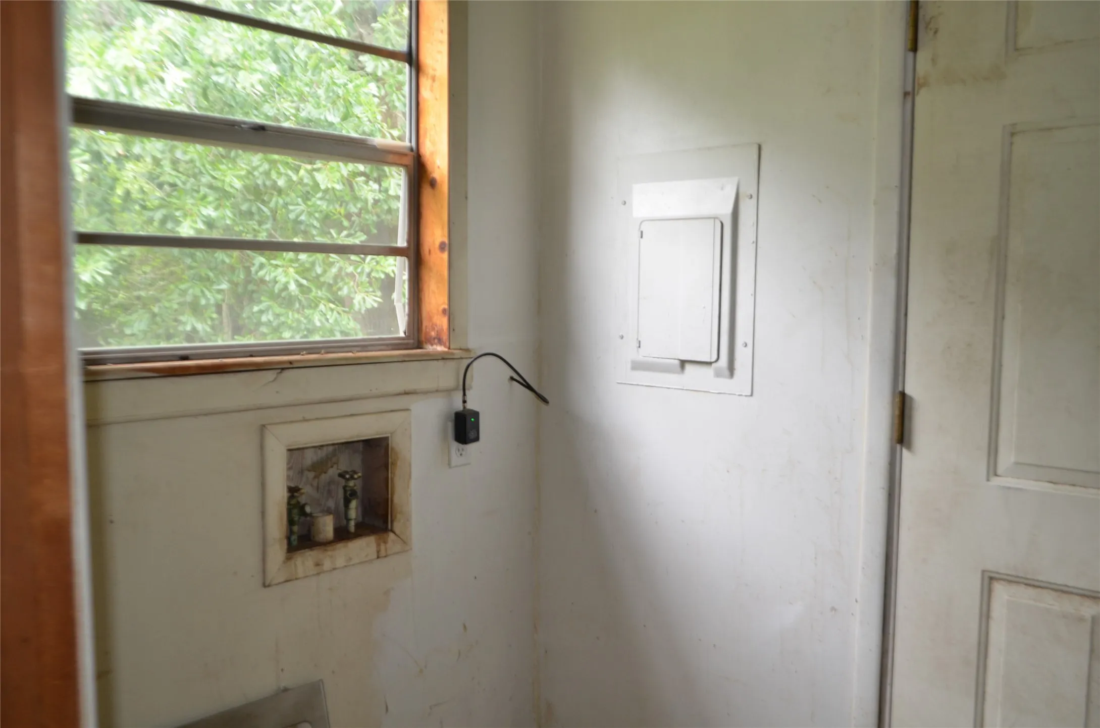 Wood-framed window with exterior views, white panel door, and wall-mounted utility access panel