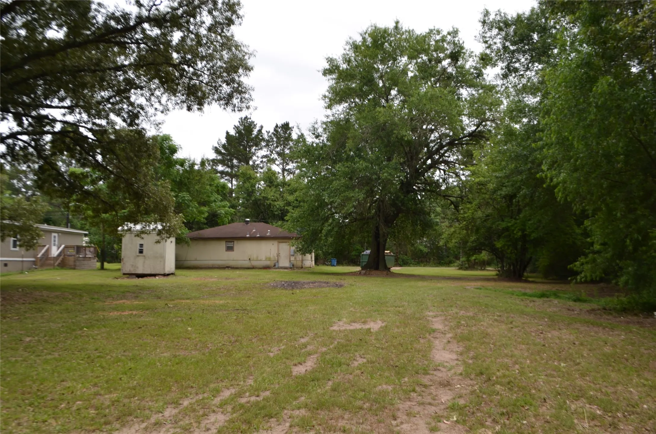 Expansive grassy lot with mature trees, a single-story residence, and an auxiliary structure