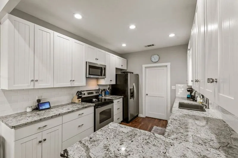 Kitchen featuring white cabinets, stainless steel appliances, decorative backsplash, light stone counters, and recessed lighting