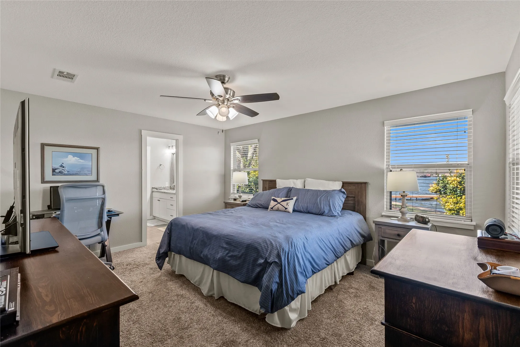 Bedroom with an office area, carpet, ceiling fan, ensuite bath, and a textured ceiling