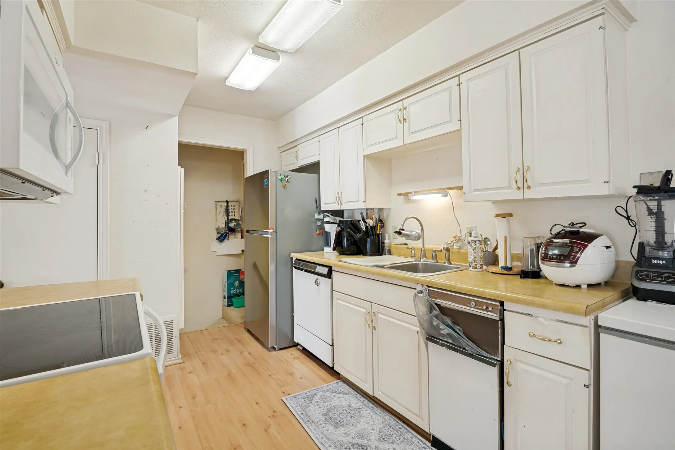 Kitchen featuring white cabinetry, wood-finish flooring, a stainless steel refrigerator, a built-in dishwasher, and a double basin sink