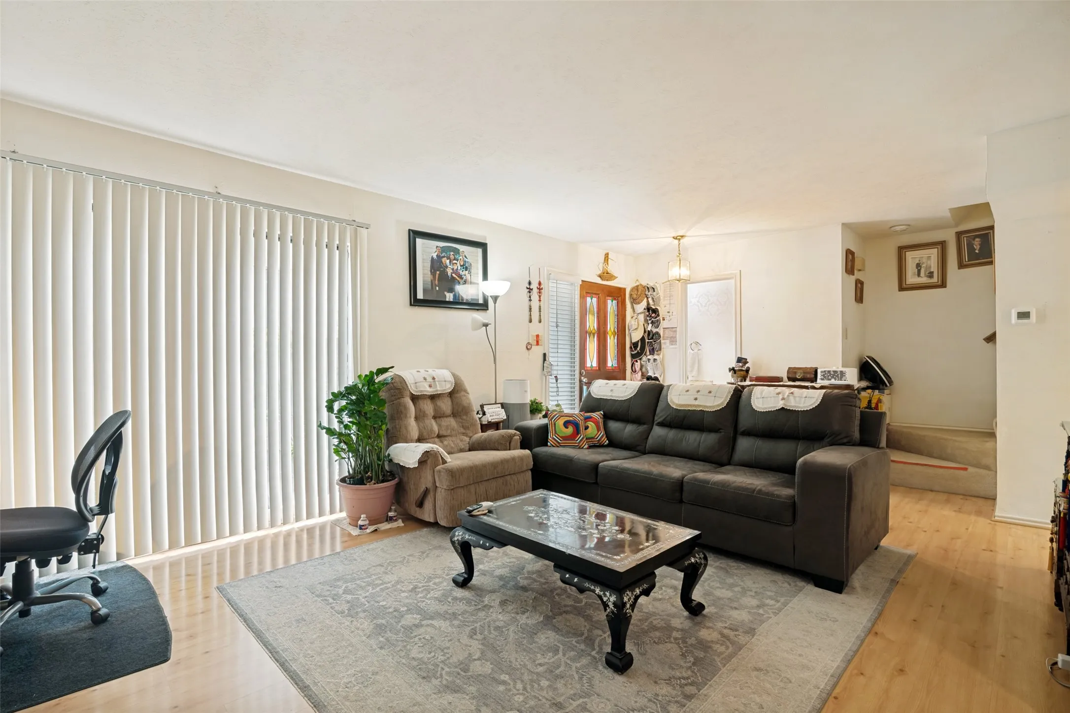 Spacious living area featuring light wood-finish flooring and a large sliding glass door with vertical blinds