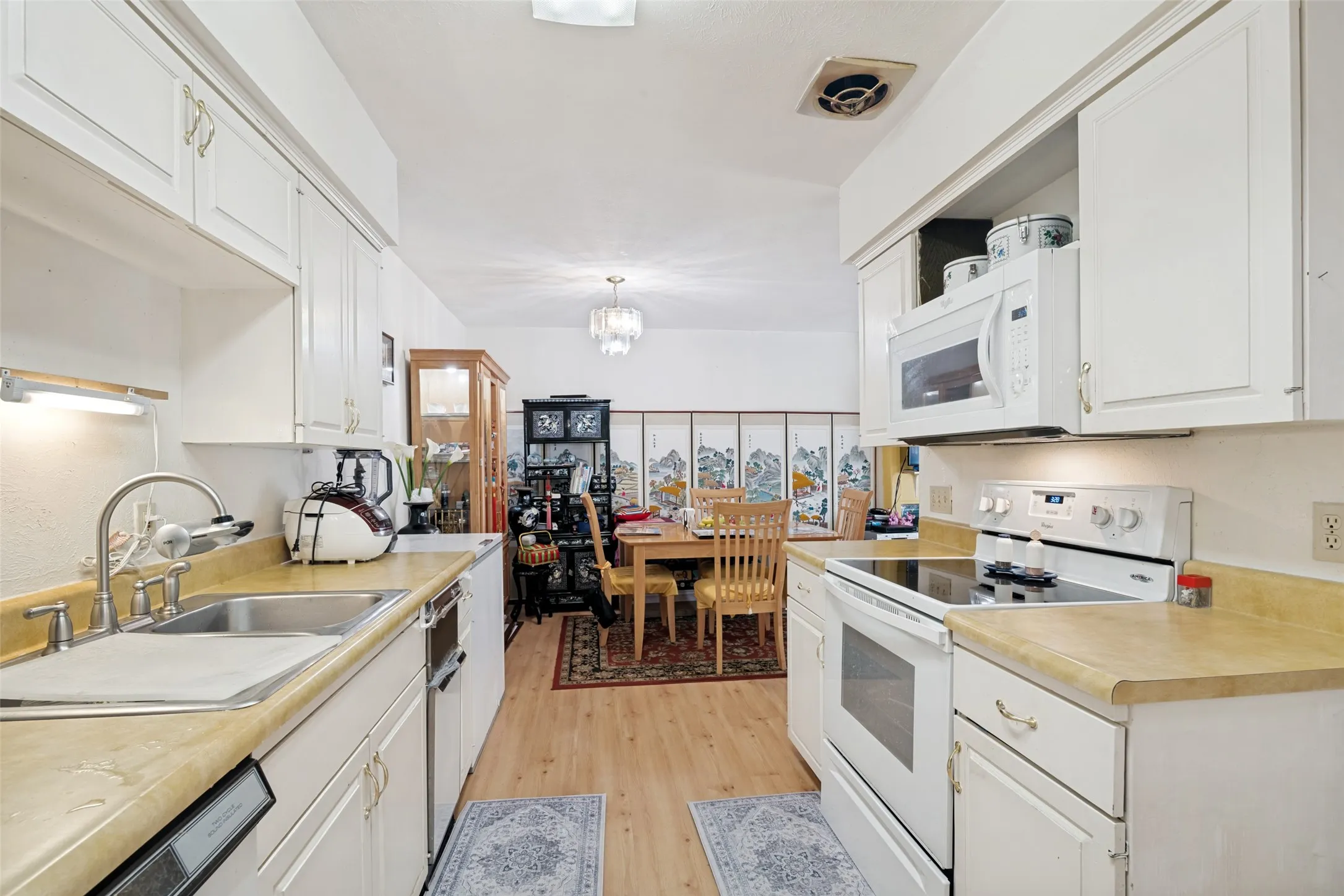 Galley kitchen featuring white cabinetry, light-toned countertops, and wood-finish flooring