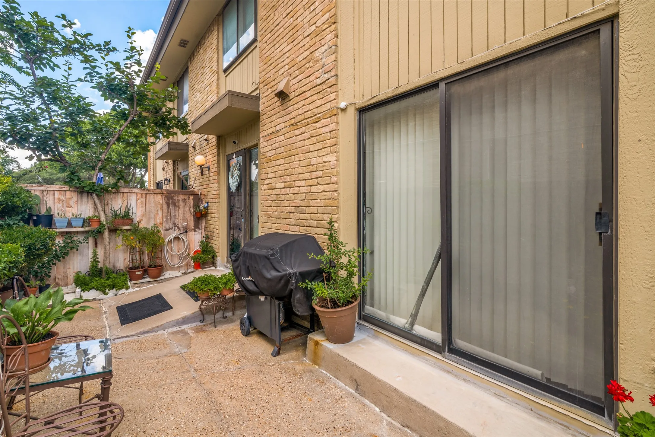 Private outdoor patio space featuring concrete flooring, a wooden privacy fence, and mature landscaping