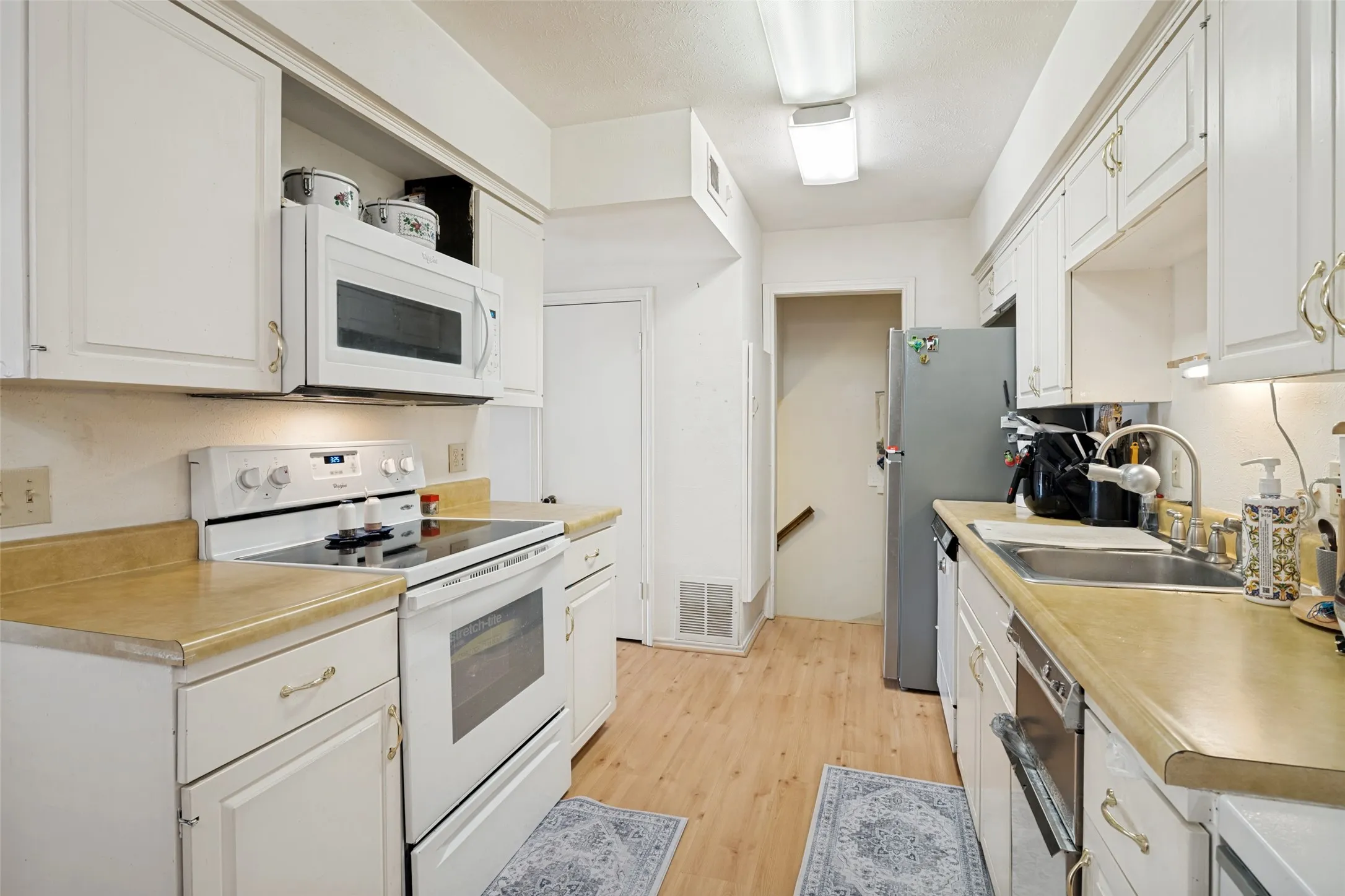 Galley kitchen featuring white cabinetry with gold-toned hardware, laminate countertops, and wood-finish flooring