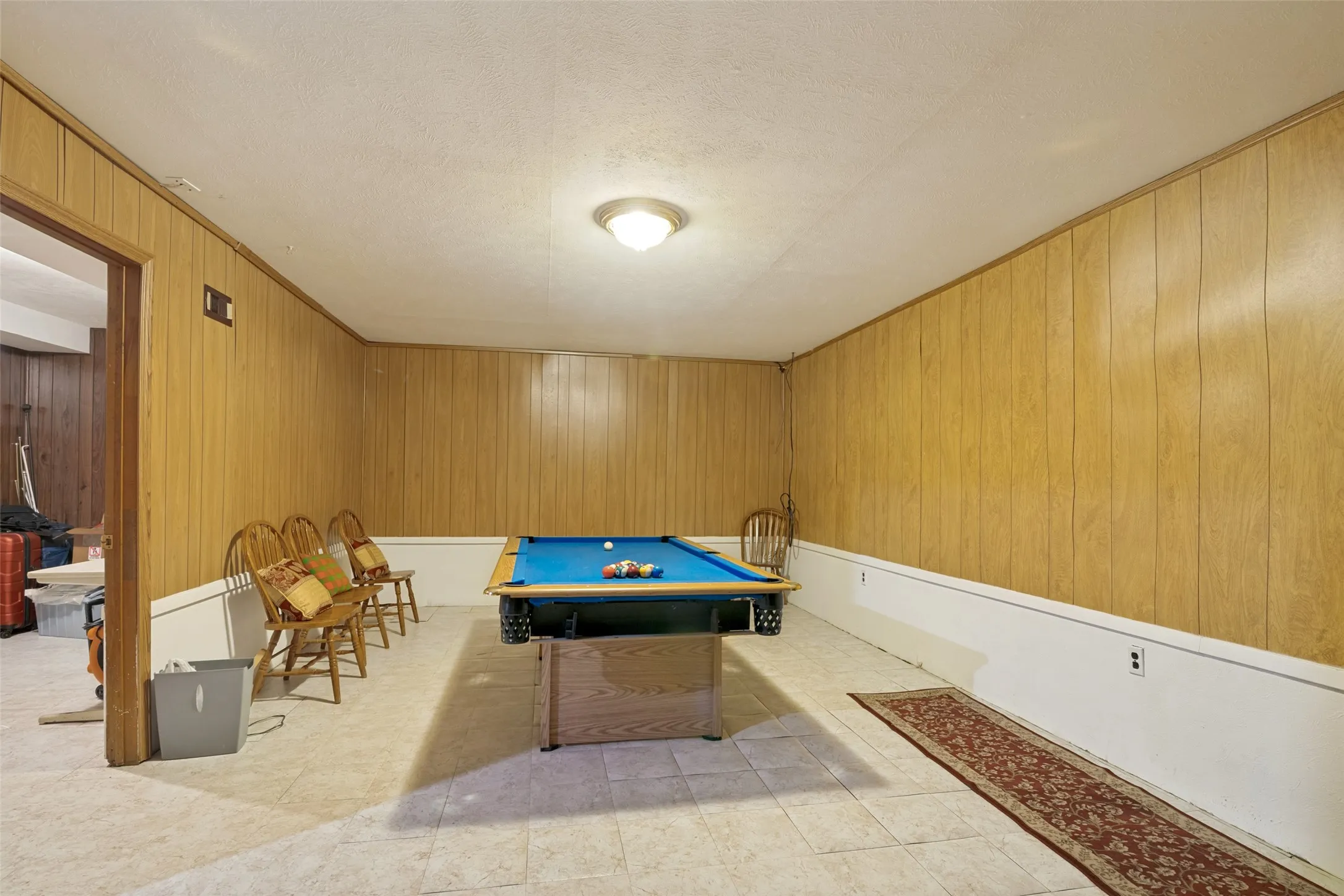 Recreation room featuring wood-panel walls, light-colored flooring, and a ceiling-mounted light fixture