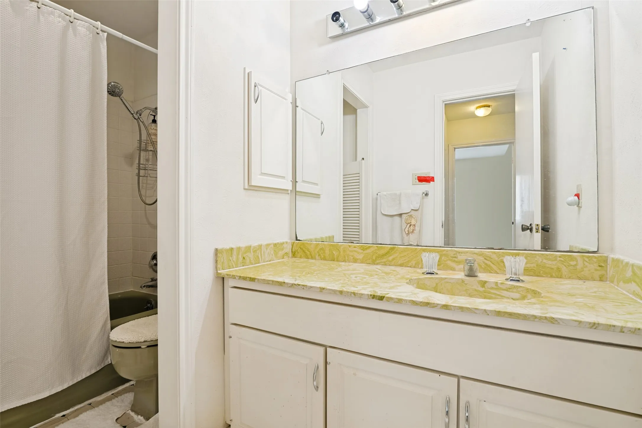 Bathroom vanity featuring a light-colored countertop with an integrated sink, under-sink cabinetry, a wall-mounted mirror, and overhead strip lighting