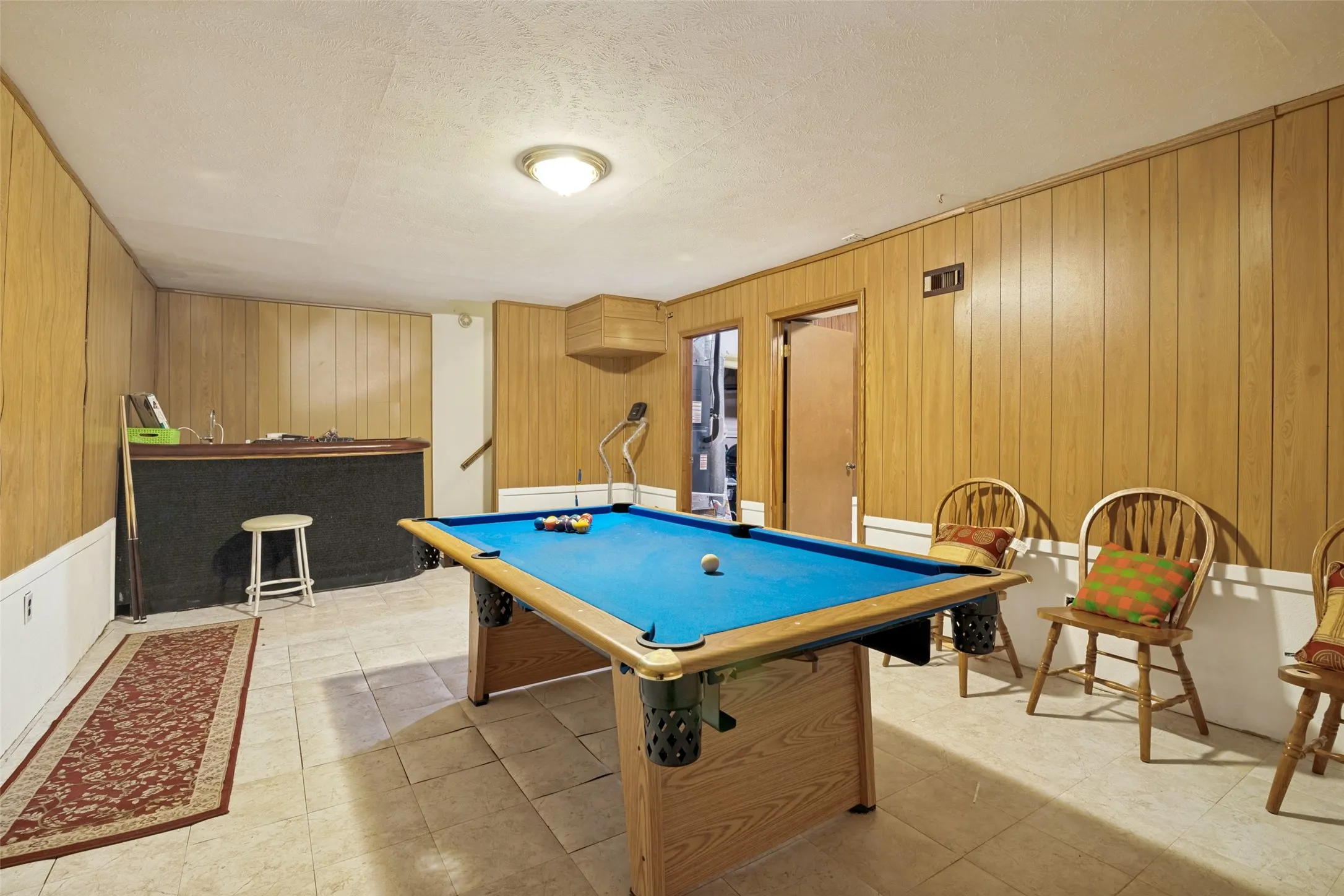 Recreation room featuring wood-panel walls and light-toned tile flooring