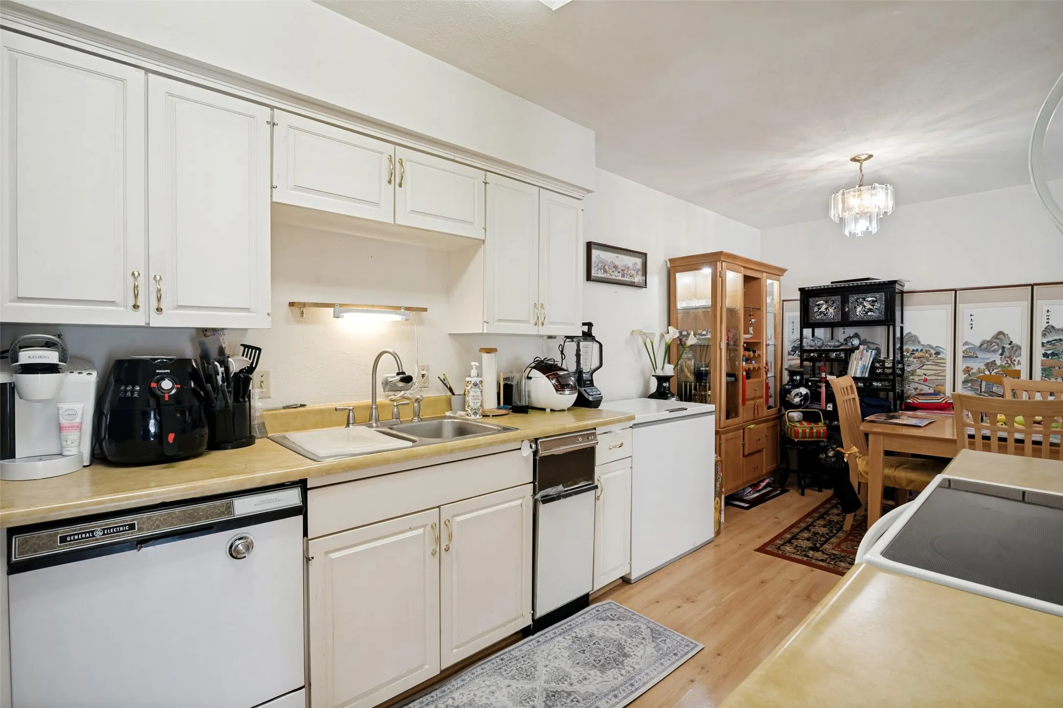 Kitchen featuring white cabinetry, a double-basin stainless steel sink, wood-finish flooring, and a crystal chandelier