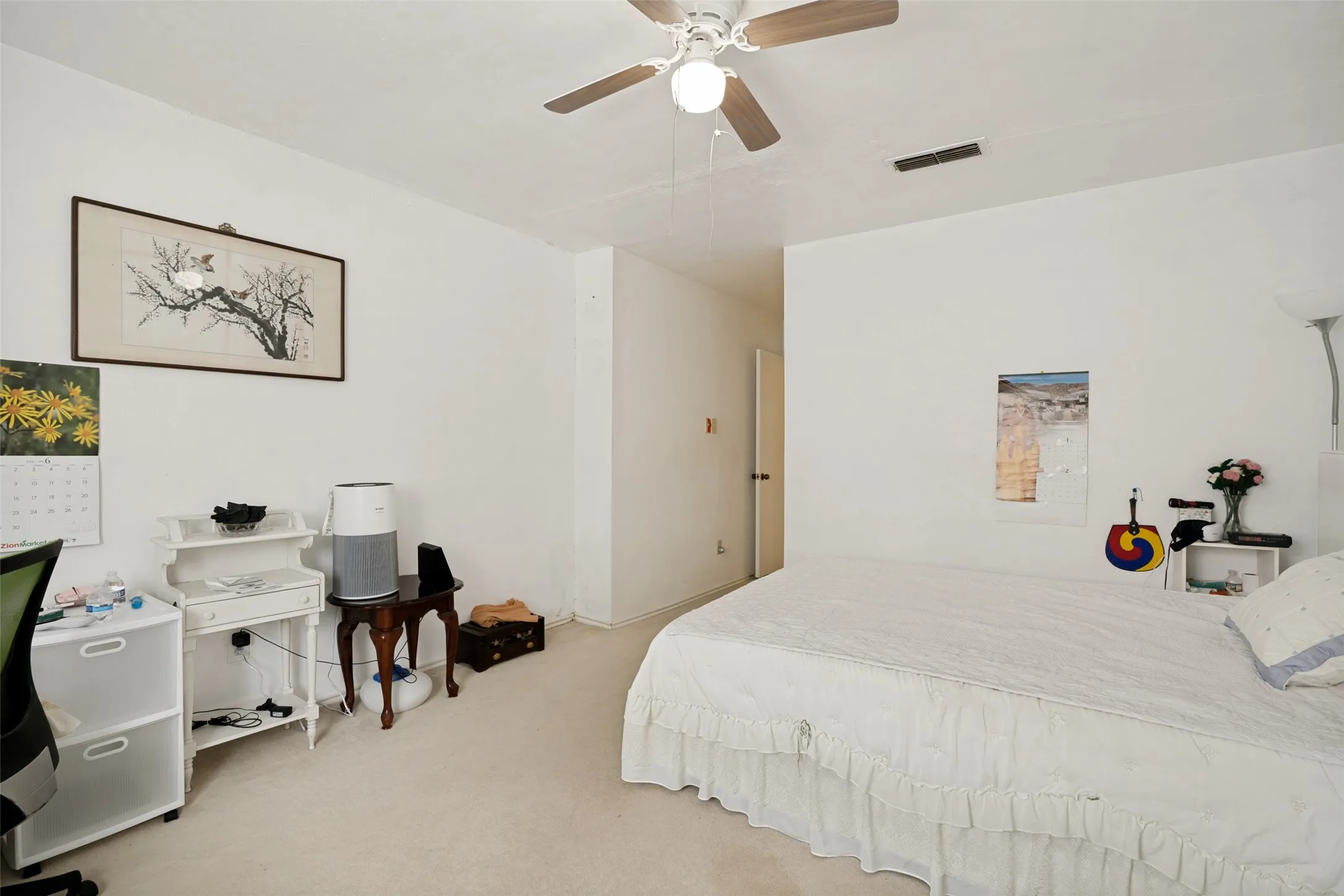 Carpeted interior space featuring white walls, a ceiling fan with light fixture, and a built-in air vent