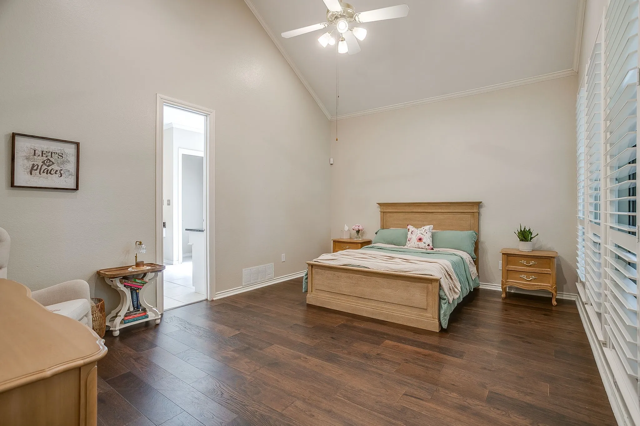 Vaulted ceiling bedroom featuring wood flooring, a ceiling fan with integrated lighting, and plantation shutters