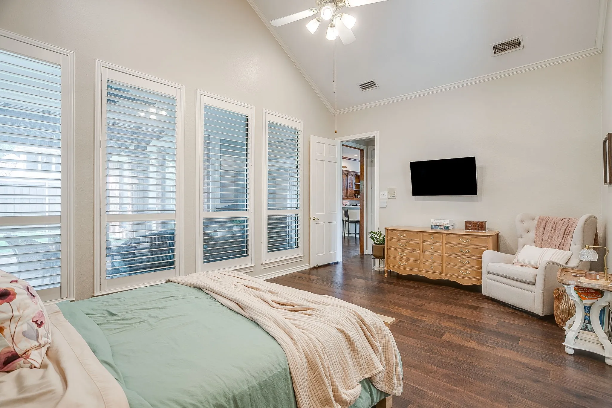 Vaulted ceiling with a ceiling fan, wood-finish flooring, and multiple tall windows with plantation shutters