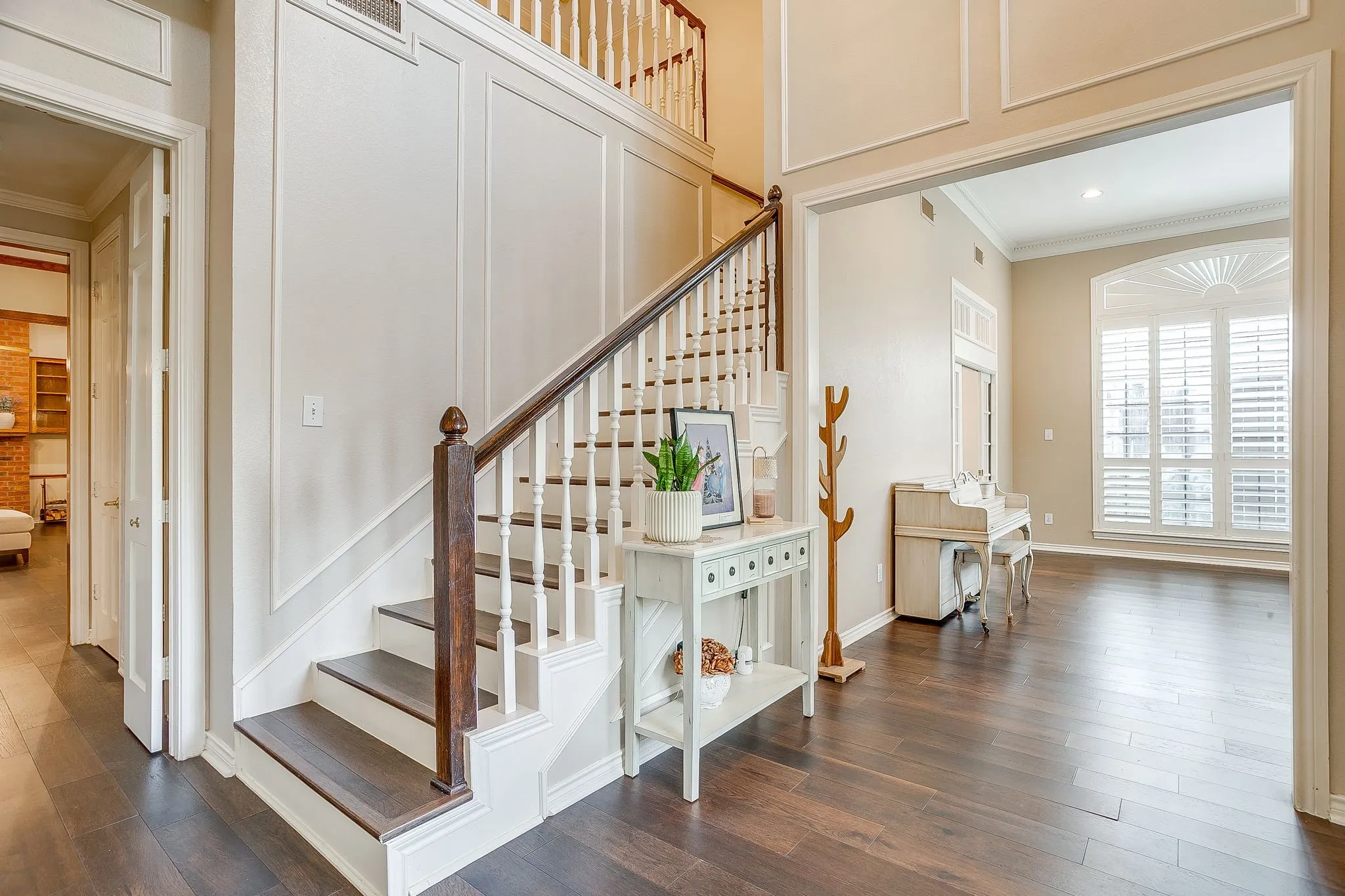 Foyer featuring a grand staircase with white risers and dark wood treads, extensive wall paneling, and a wide entryway leading to a formal living room with a large arched window with plantation shutters