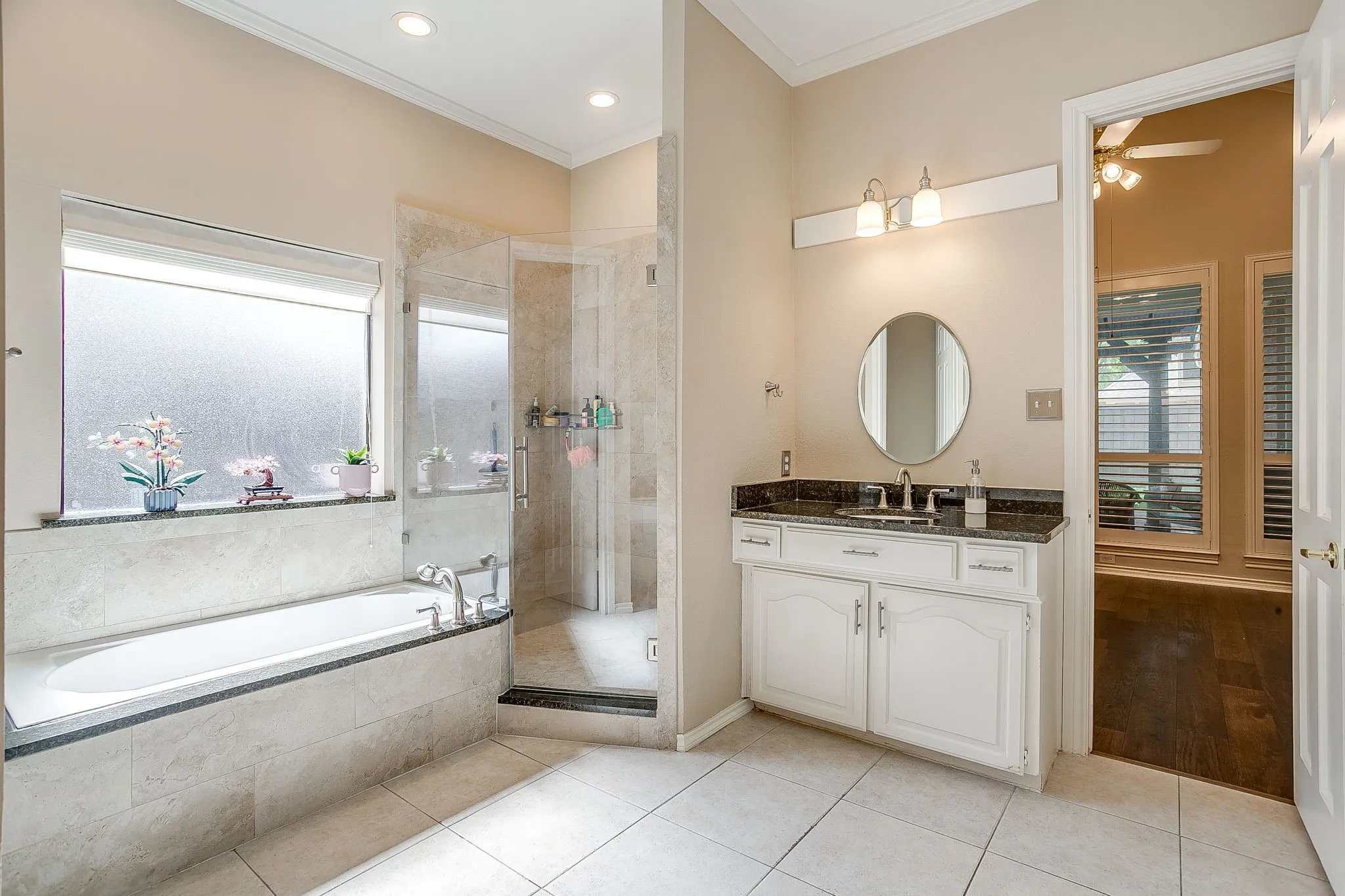 Spacious bathroom featuring a built-in bathtub, a walk-in shower with clear glass enclosure, a vanity with dark countertop and white cabinetry, recessed lighting, and tile flooring
