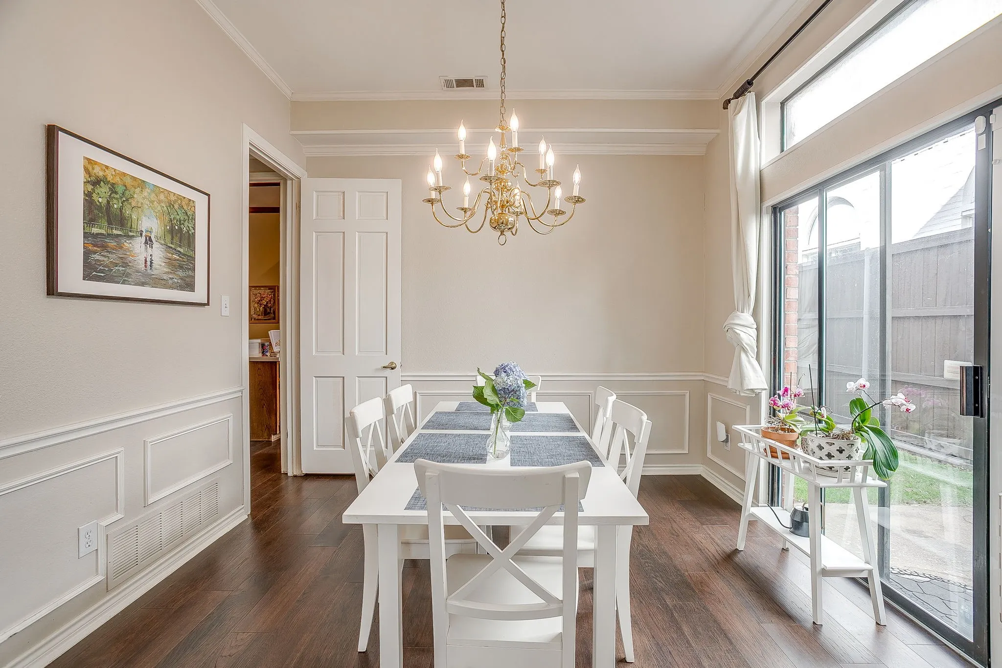 Dining area featuring dark wood flooring, wainscoting, crown molding, chandelier and a slider