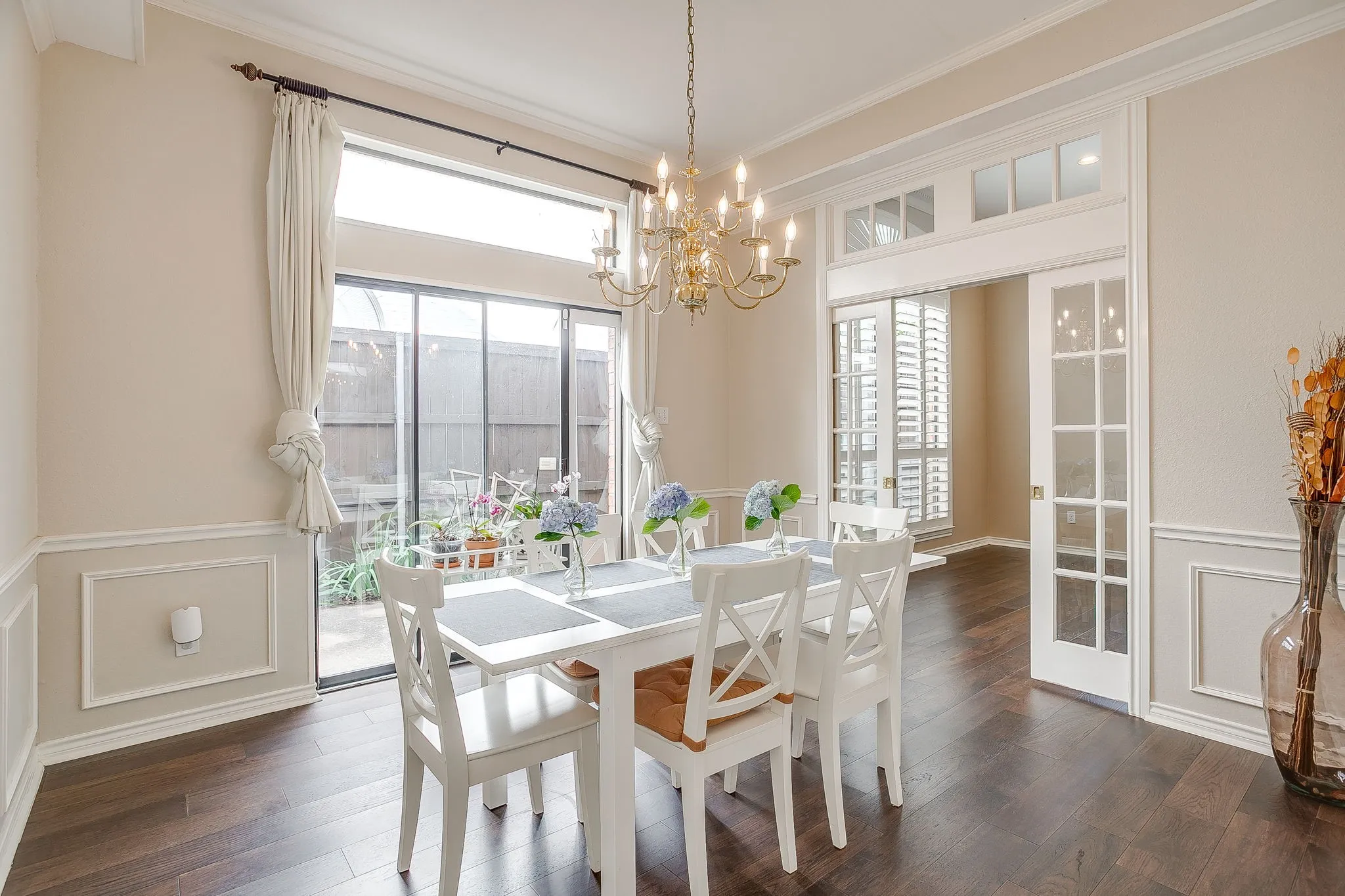Dining room featuring wood flooring, wainscoting, crown molding, slider, and a brass chandelier