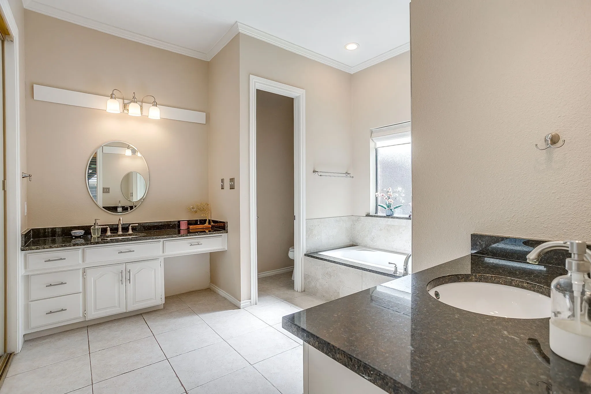 Bathroom featuring dual vanity areas with dark granite countertops, white cabinetry, and white tile flooring