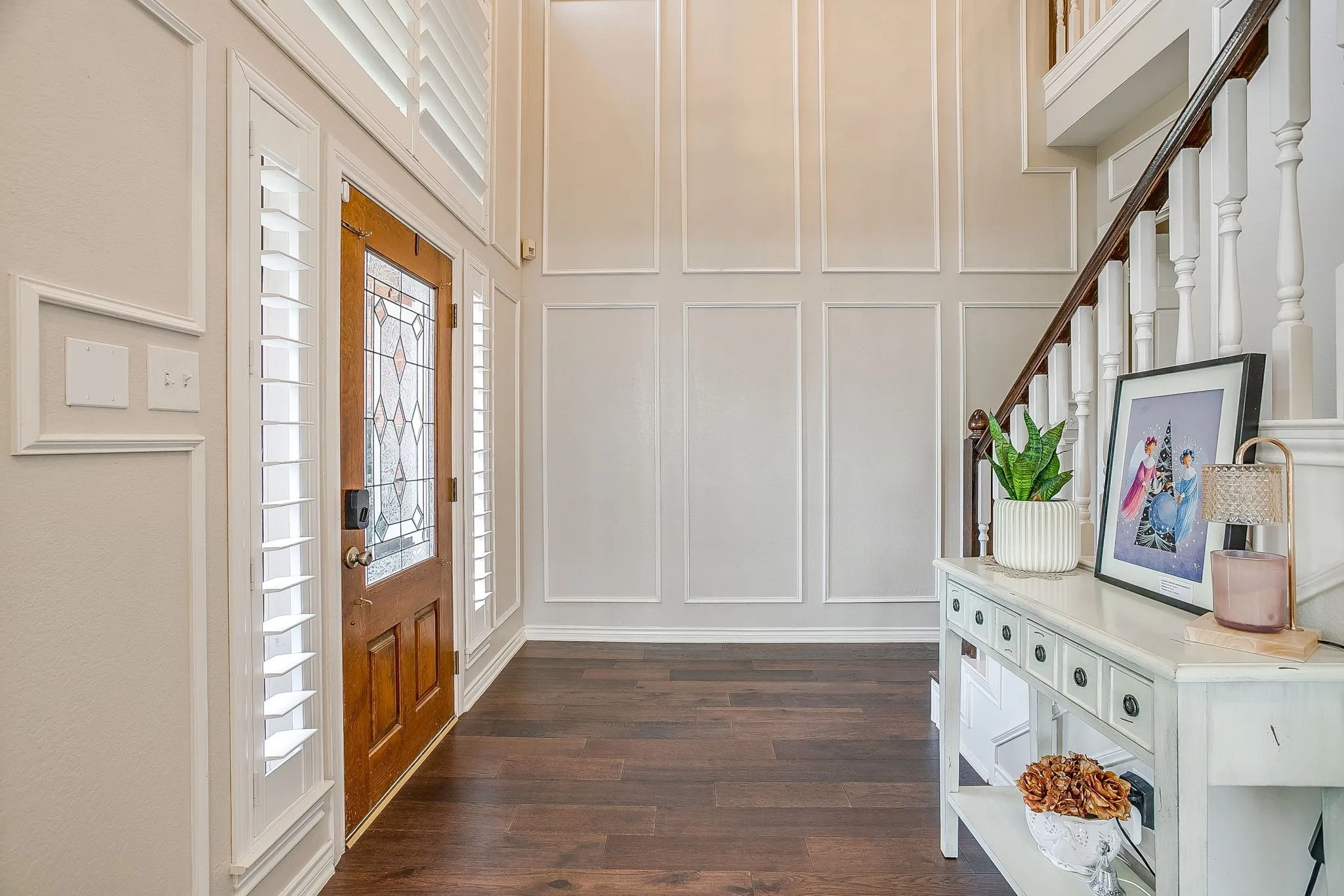Two-story foyer featuring engineered hardwood flooring, a wood-paneled entry door with leaded glass, white plantation shutters, and extensive wall molding