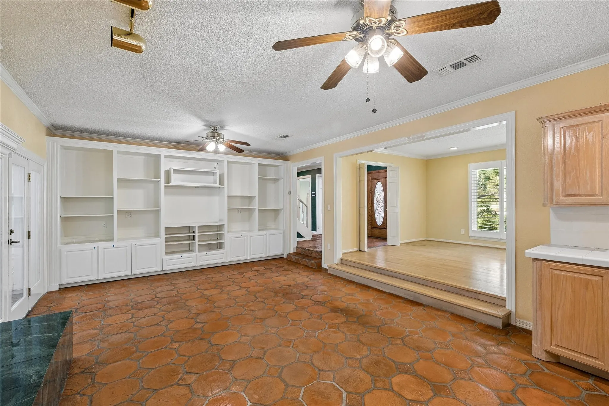 Spacious room featuring hexagonal terracotta-style flooring and a full wall of white built-in cabinetry with open shelving and lower cabinets