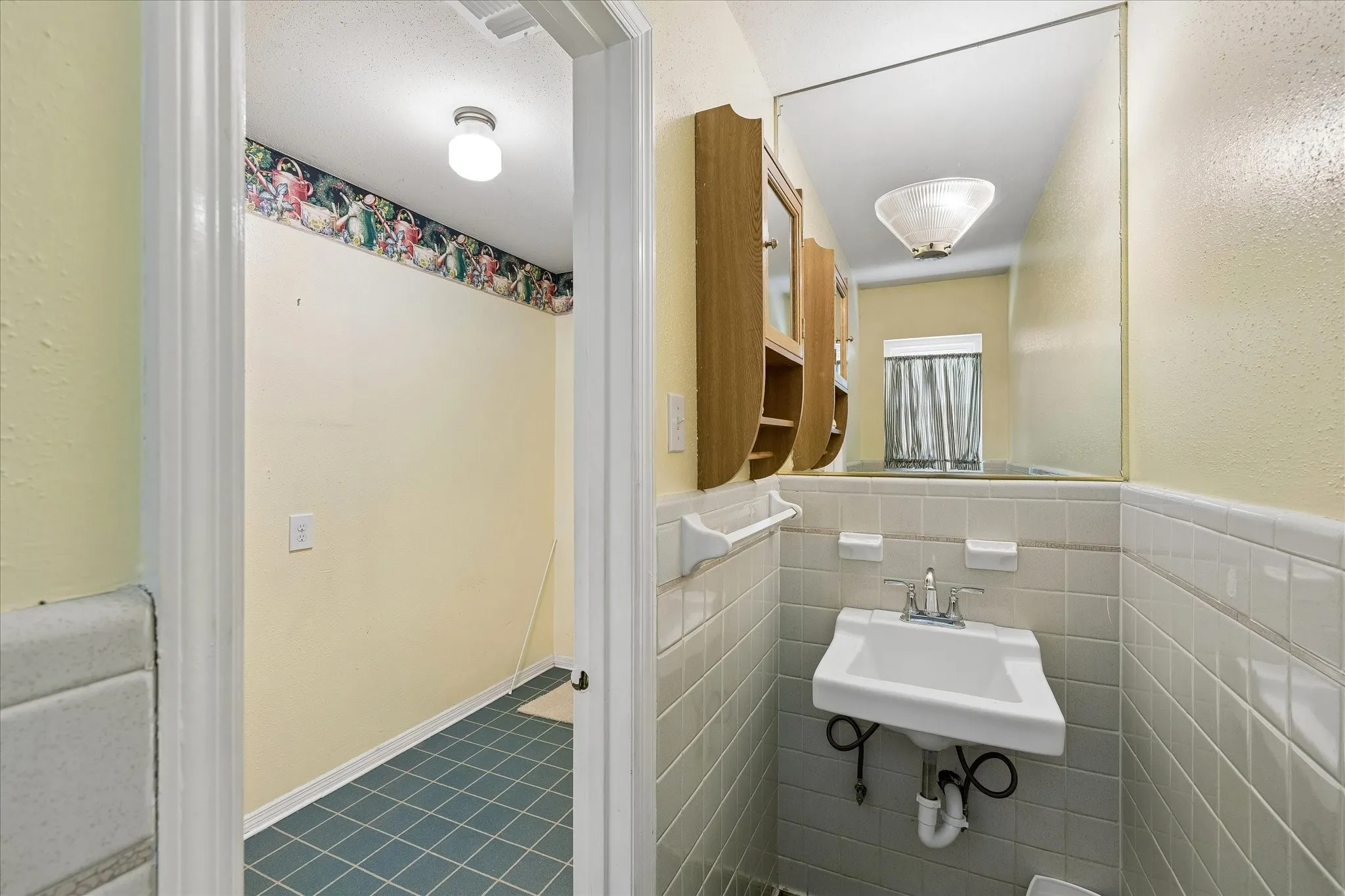 Bathroom featuring a pedestal sink with chrome faucet, a large wall-mounted mirror, and white tiled walls