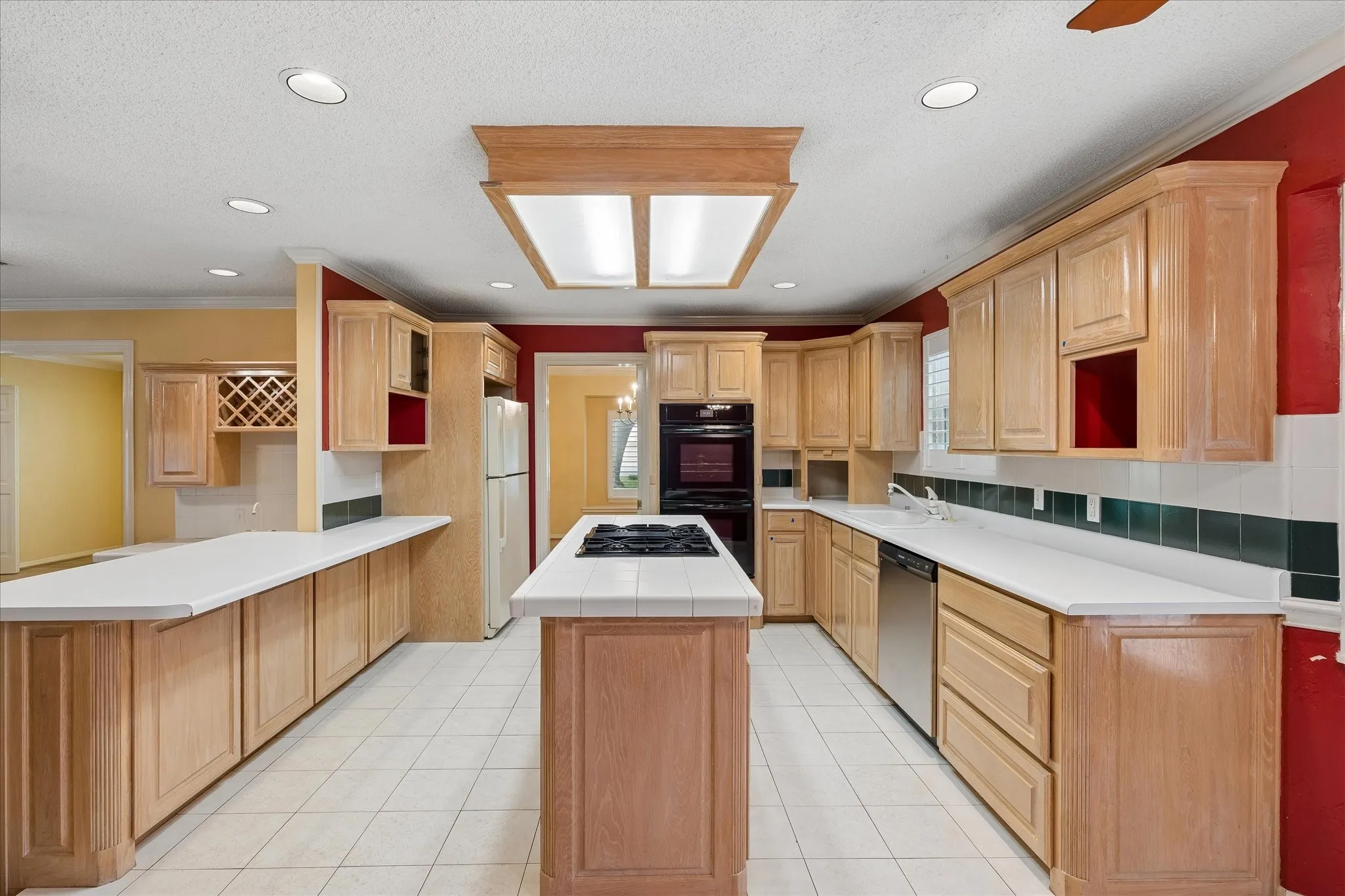 Kitchen featuring light wood-finish cabinetry, a central island with a built-in cooktop, white tile flooring, recessed ceiling lighting, and stainless steel appliances