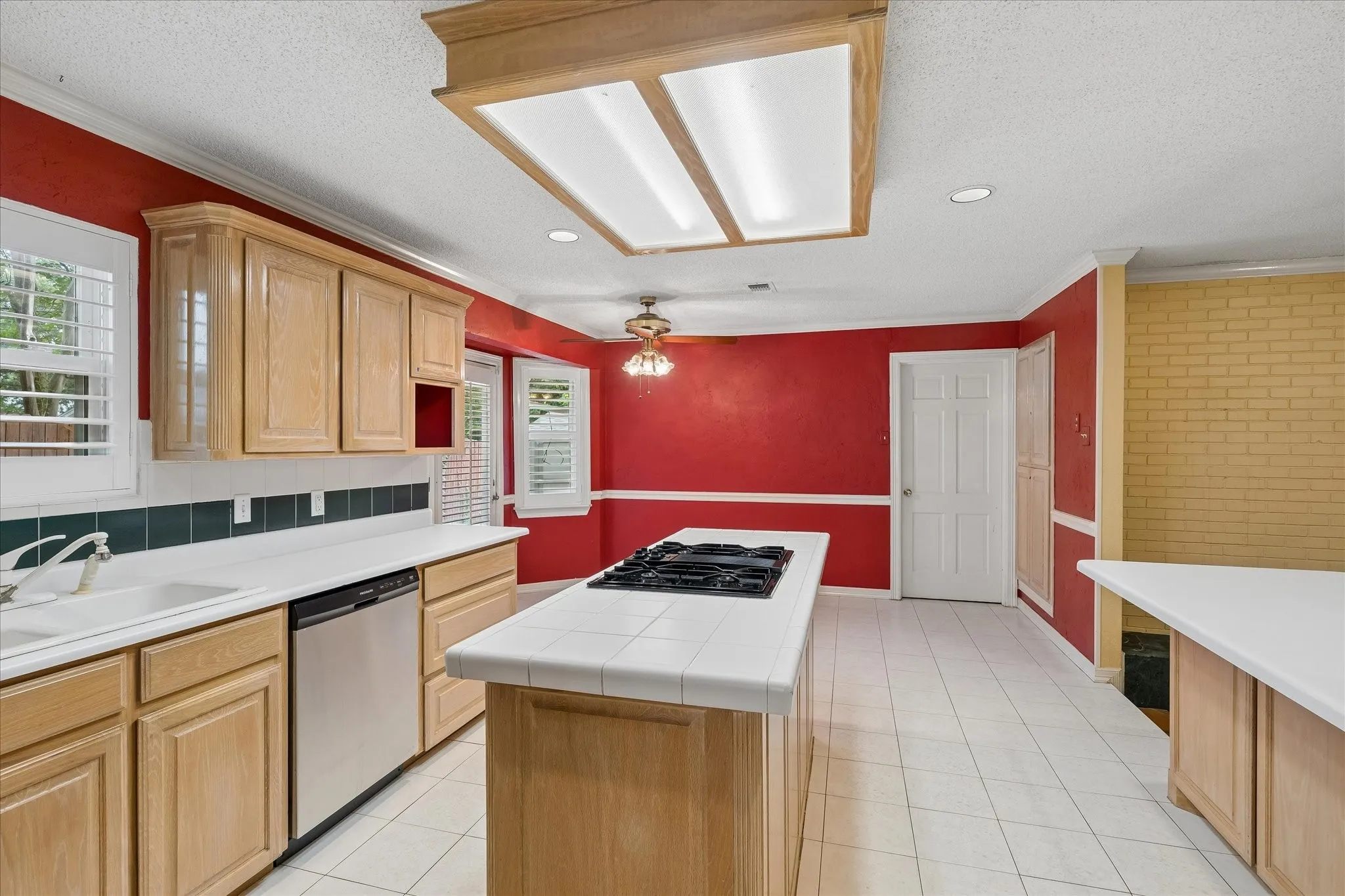 Kitchen featuring light wood cabinetry, white tile flooring, and a central island with a built-in cooktop