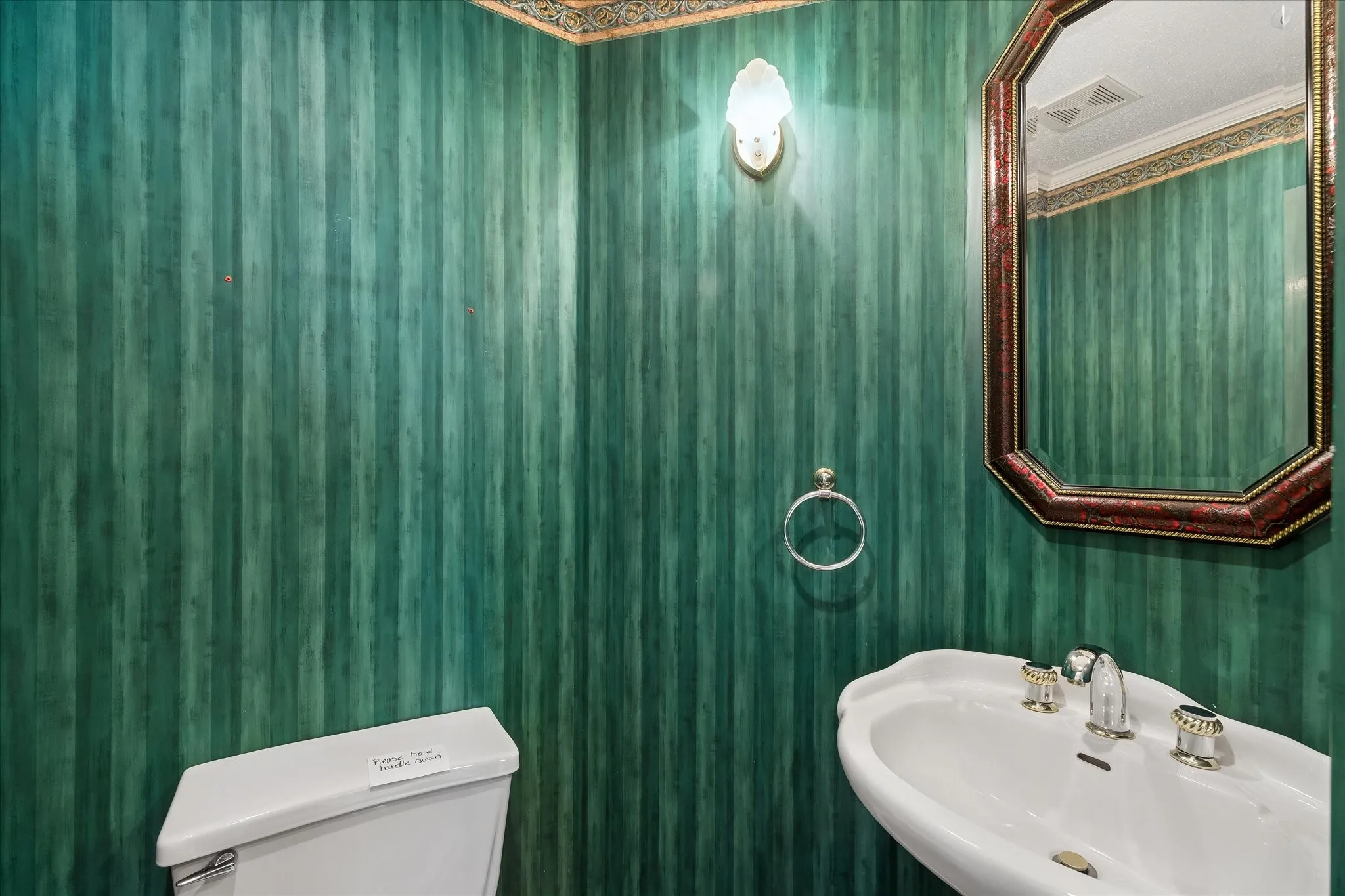 Powder room featuring a pedestal sink with decorative fixtures, an octagonal framed mirror, and a wall-mounted light fixture
