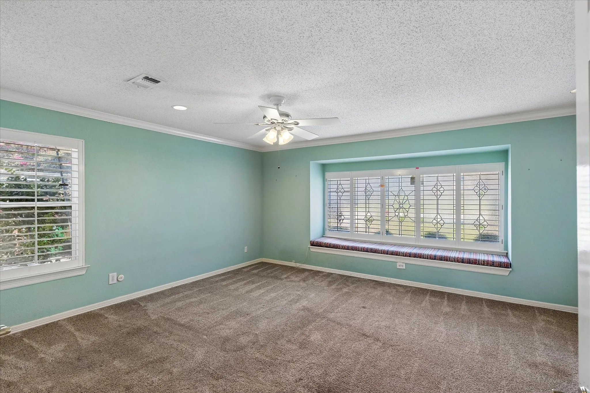 Spacious room featuring a deep window seat with a patterned cushion, white plantation shutters, and a ceiling fan with integrated lighting