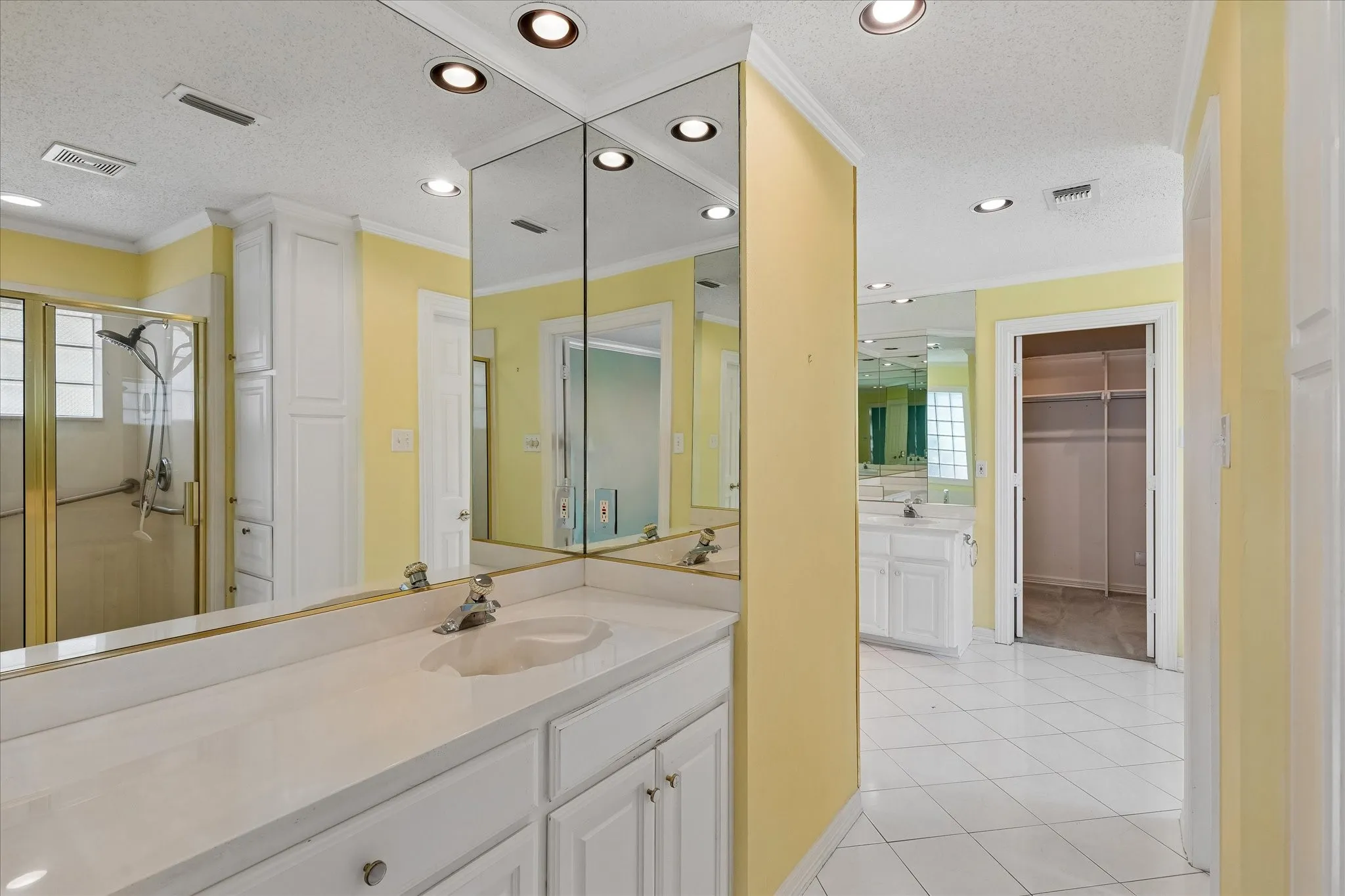 Bathroom featuring dual vanities with white cabinetry, integrated sinks, and expansive mirrors