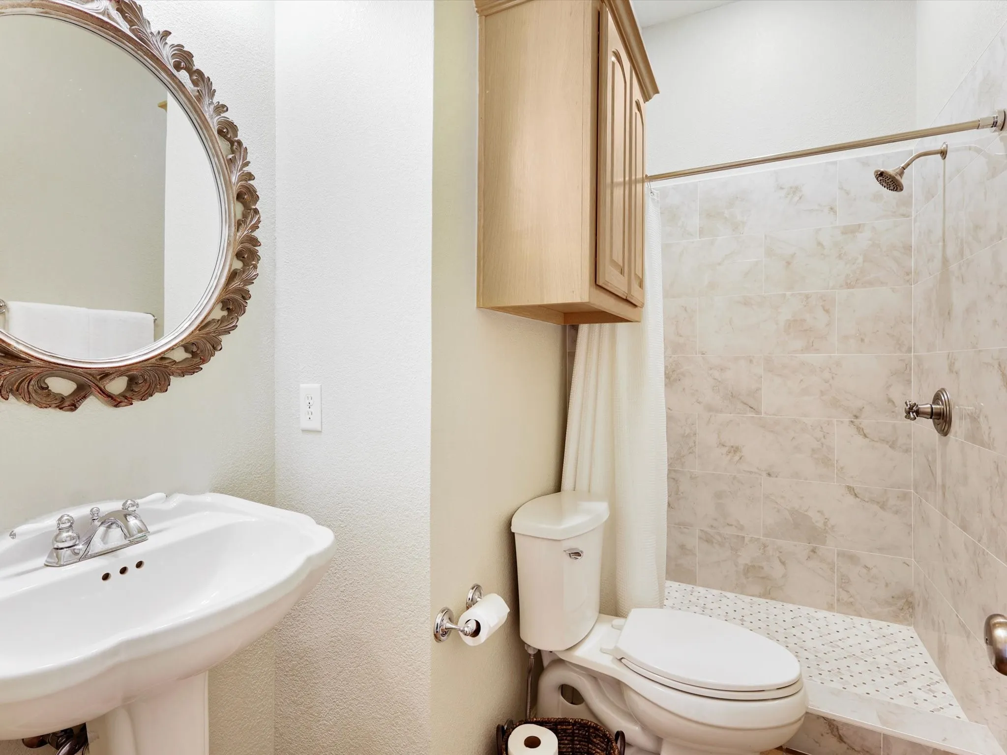 Bathroom featuring a pedestal sink, ornate framed mirror, and a tiled shower with a mosaic floor