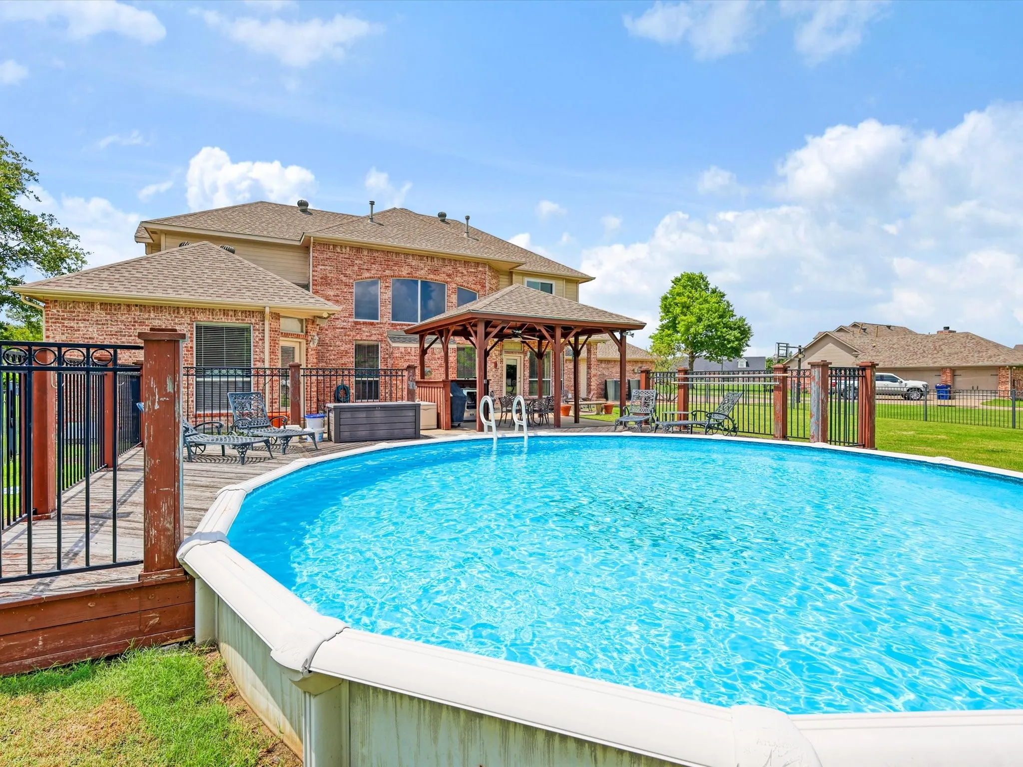 Backyard featuring an above-ground pool with surrounding wood decking and black metal fencing