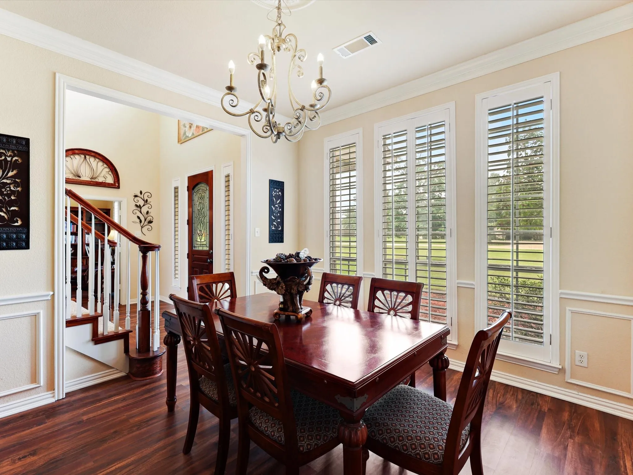 Formal dining area featuring rich wood-finish flooring, white plantation shutters, and a classic chandelier