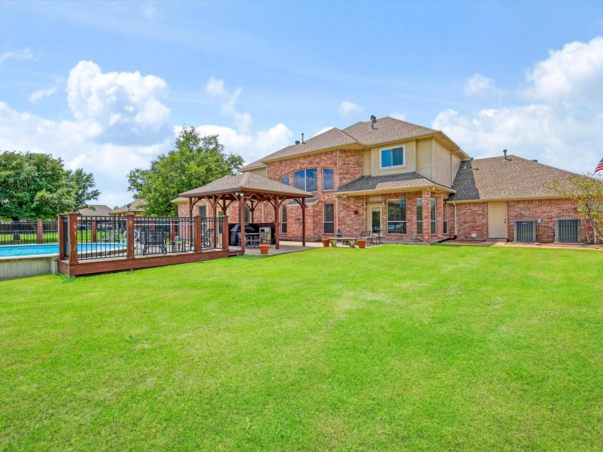 Spacious backyard featuring a large green lawn, an in-ground swimming pool, and a wooden deck with a built-in gazebo