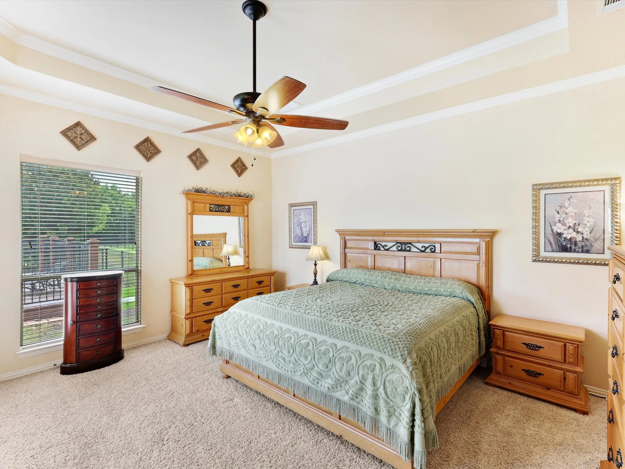 Spacious room featuring tray ceilings, neutral carpeting, and a large window with horizontal blinds