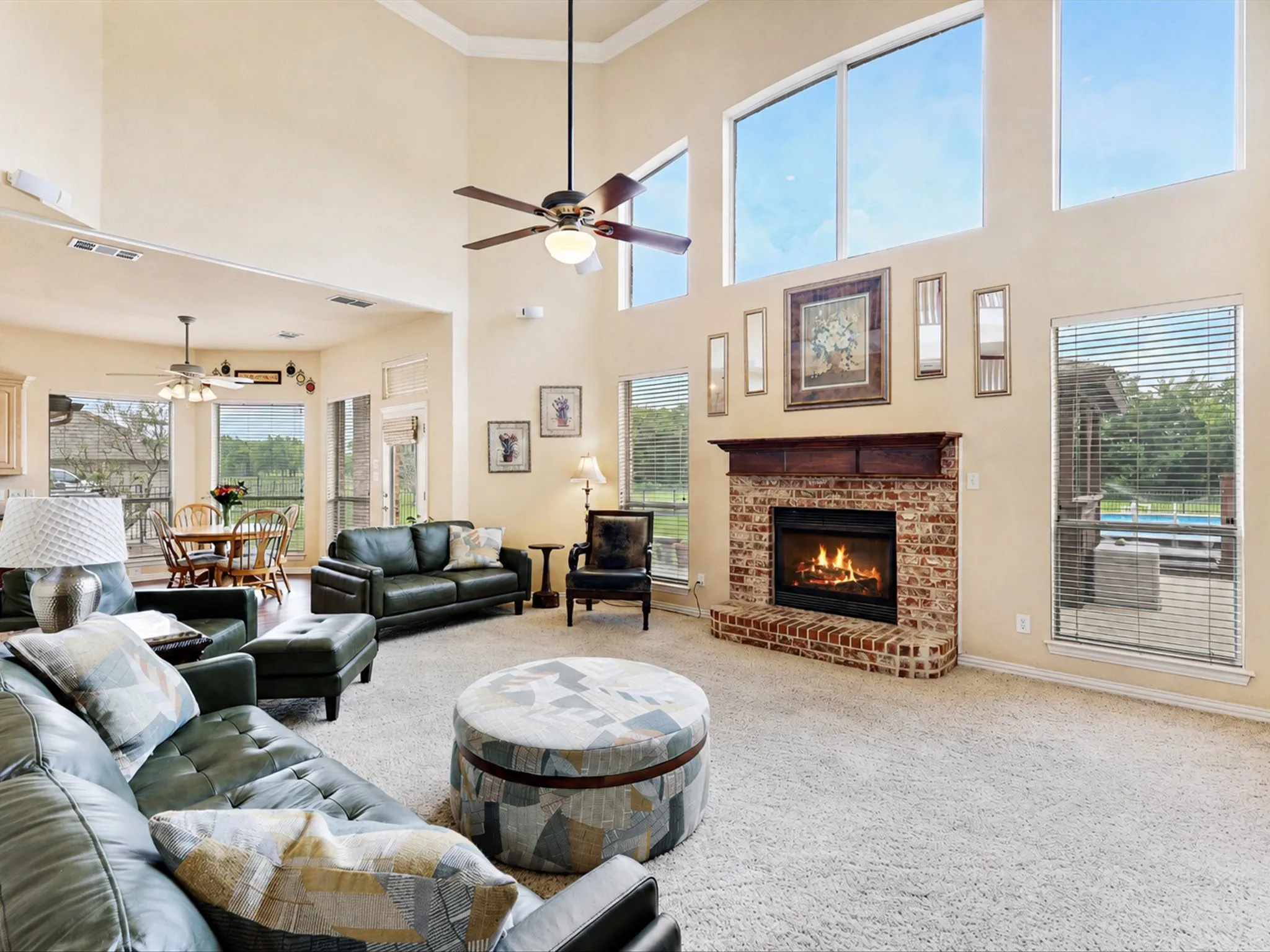 Two-story living area featuring a brick fireplace with a wood mantle, high ceilings, large upper windows, and a ceiling fan
