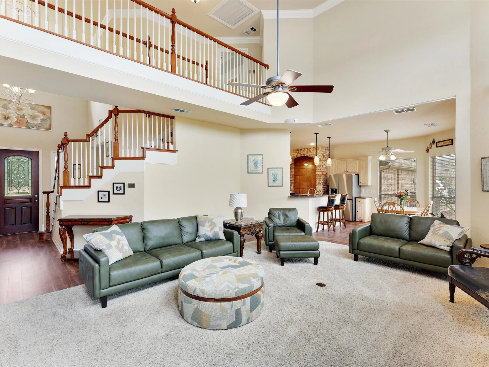 Open-concept living area featuring high ceilings, a second-story balcony with white balusters, and a staircase with wood-finish treads