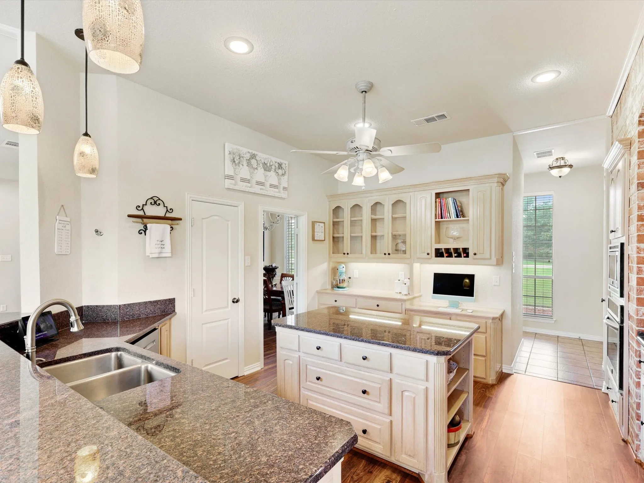 Kitchen featuring an island with built-in storage, granite countertops, stainless steel double basin sink, wood-finish flooring, and cream-colored cabinetry