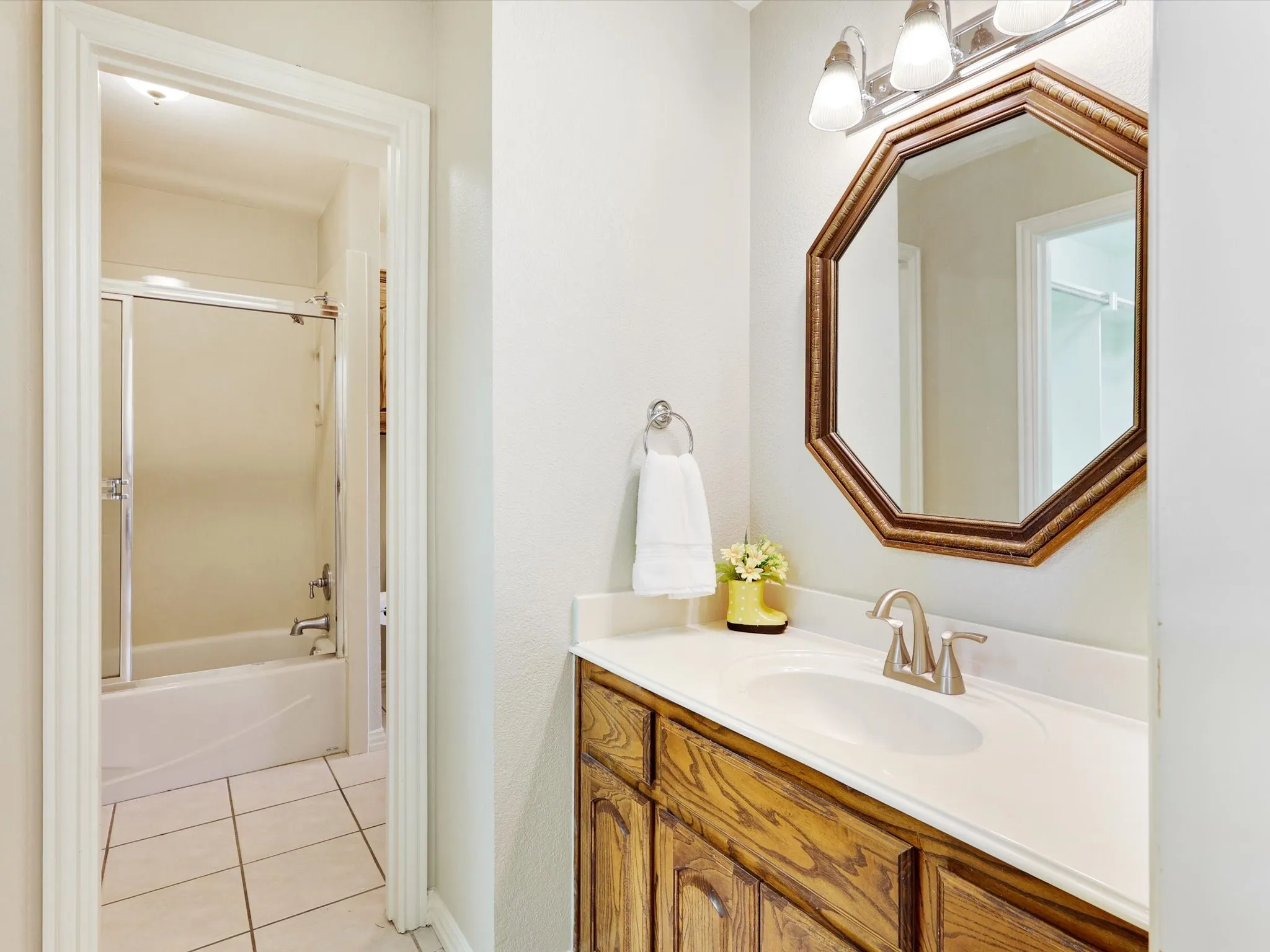Bathroom vanity featuring a wood-finish cabinet, white countertop with an integrated sink, brushed nickel faucet, and an octagonal framed mirror